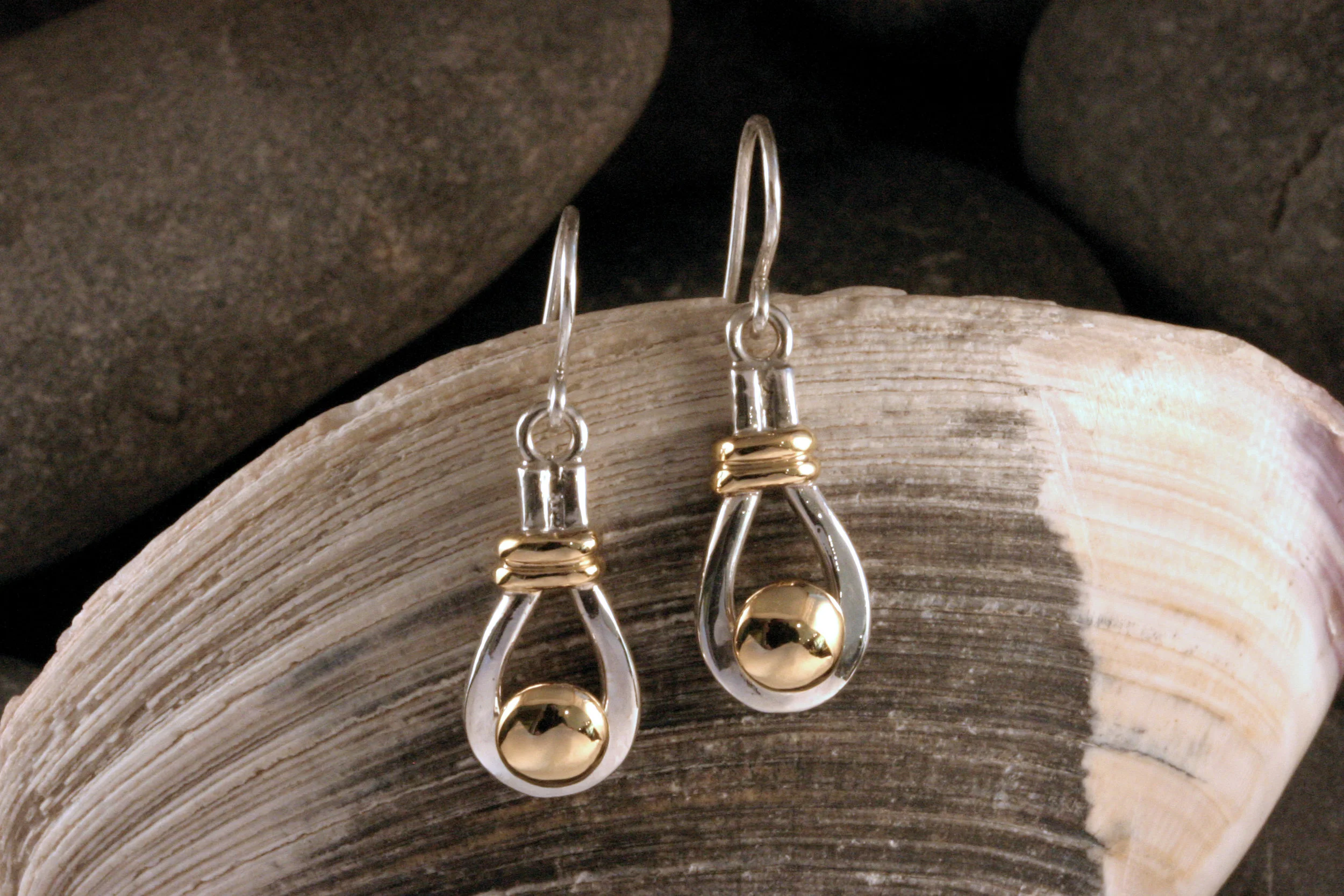 Sterling silver and 14K gold button dangle earrings on a seashell