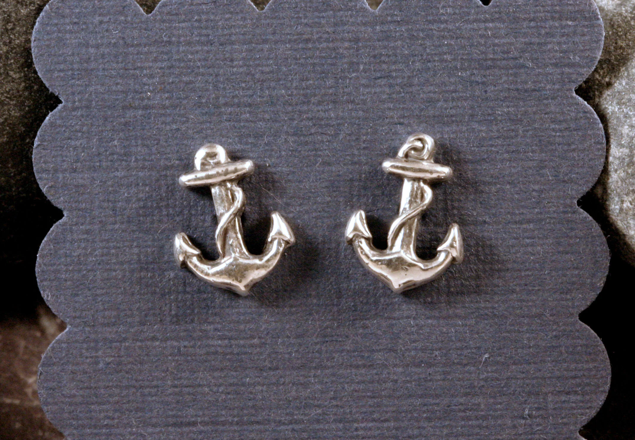 Oxidized sterling silver miniature anchor stud earrings on blue paper