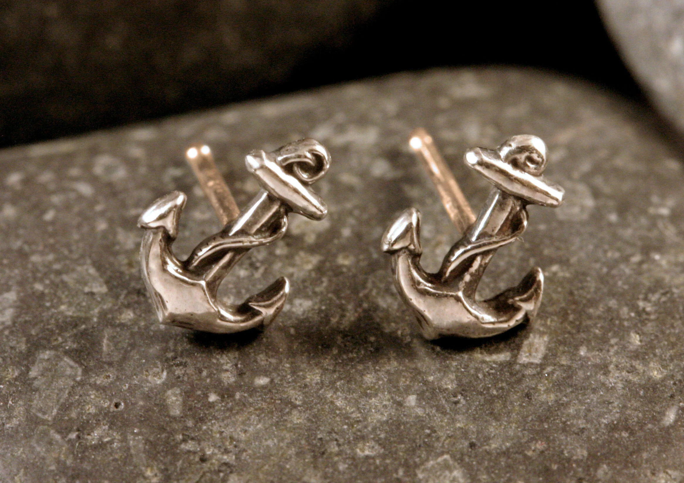 Oxidized sterling silver miniature anchor stud earrings with 14K gold posts on a rock