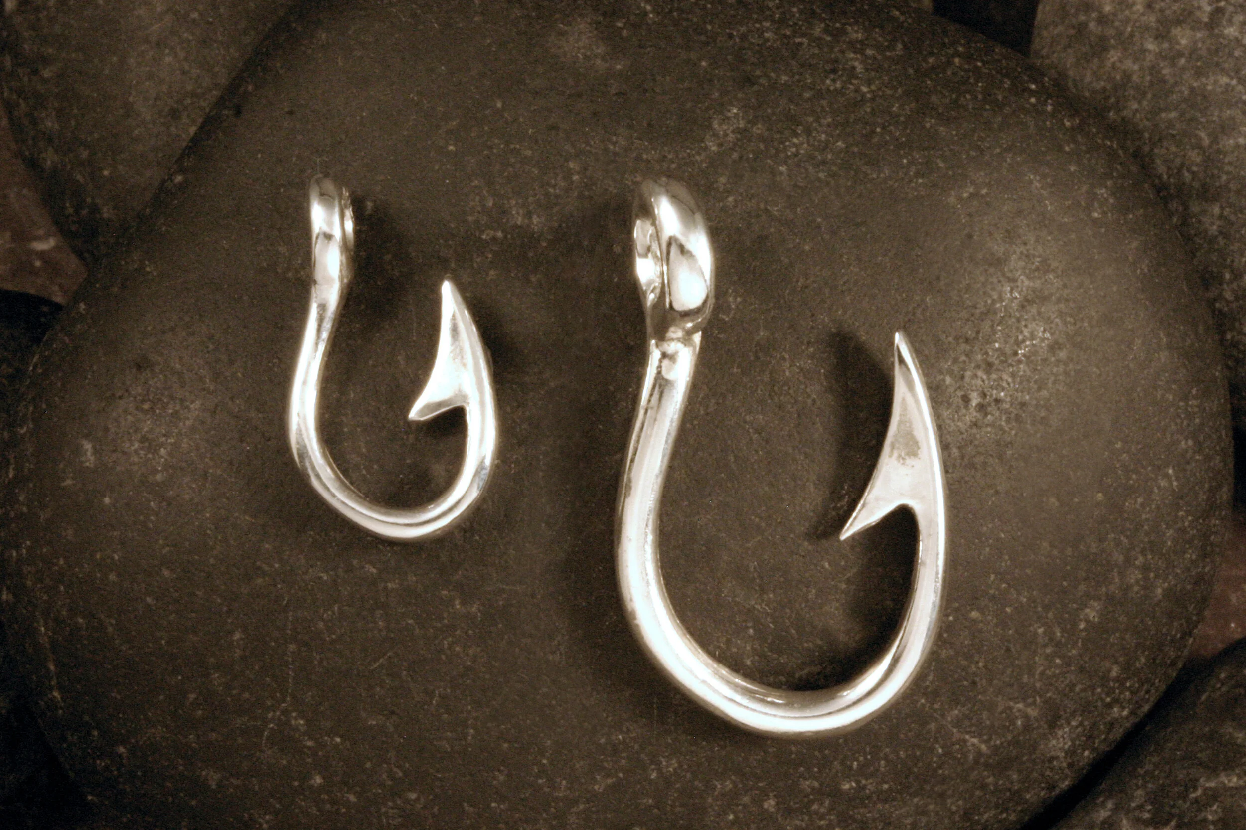 Medium and large sterling silver cod fish hook pendants next to each other.