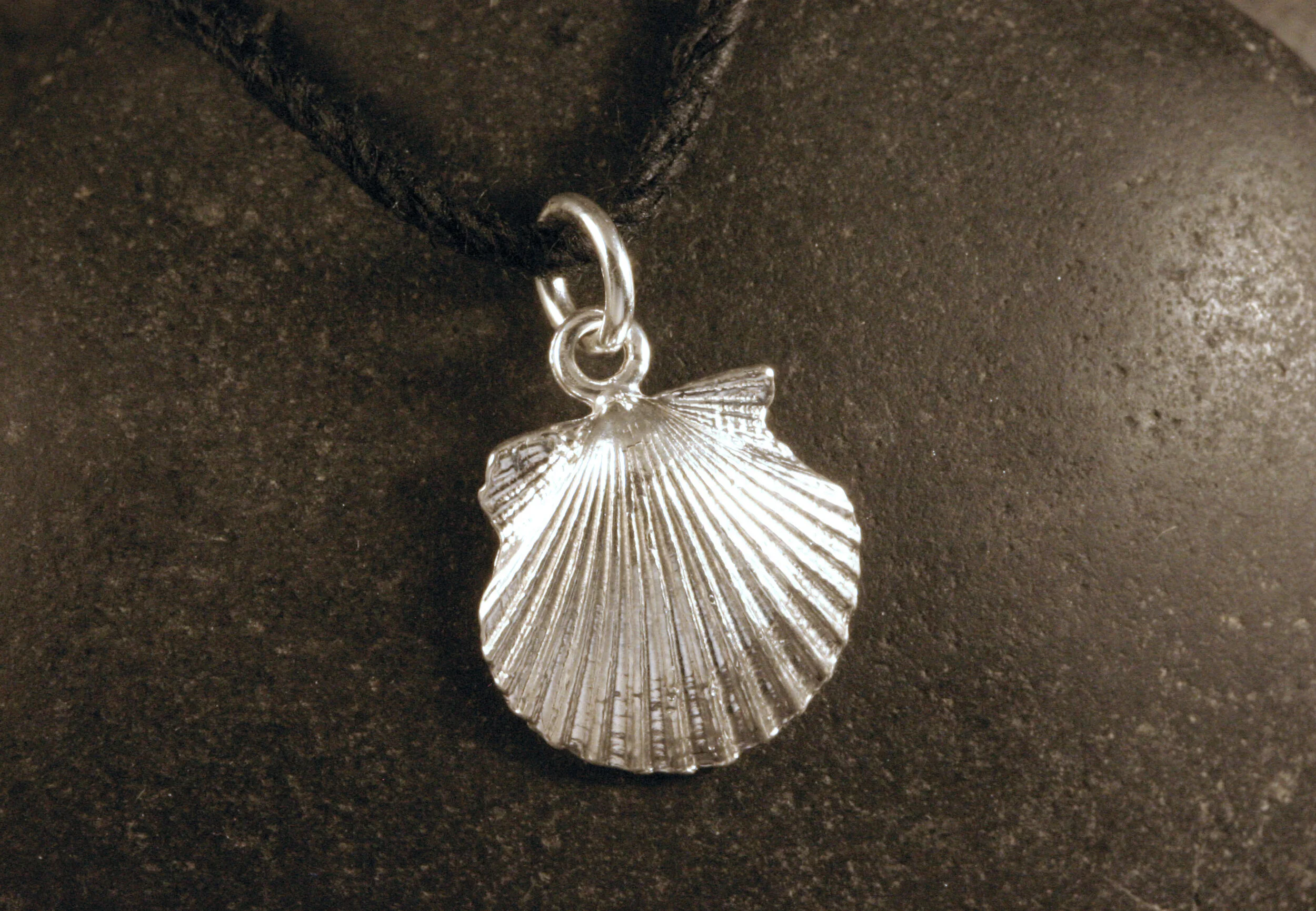 Angled view of small shiny sterling silver scallop seashell charm