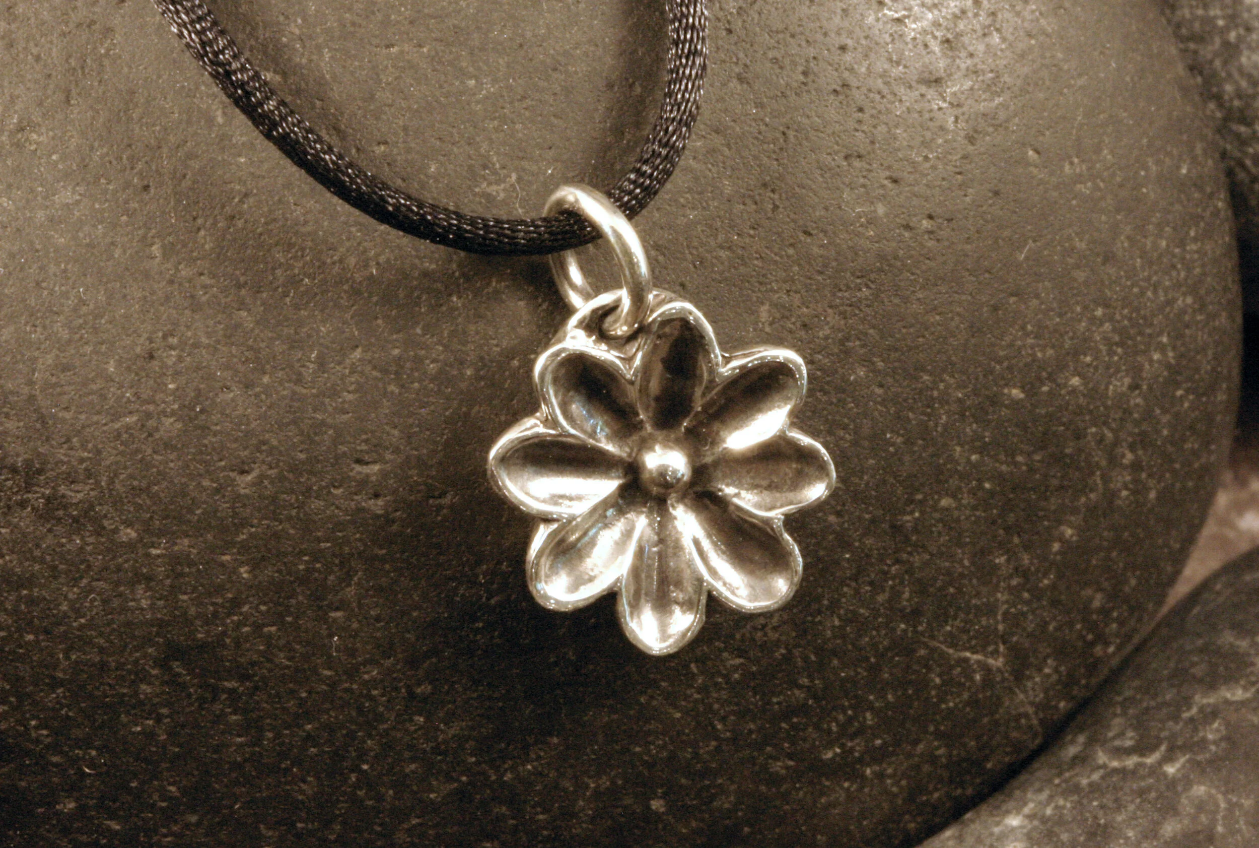 Oxidized sterling silver daisy flower charm pendant on black cord angled view