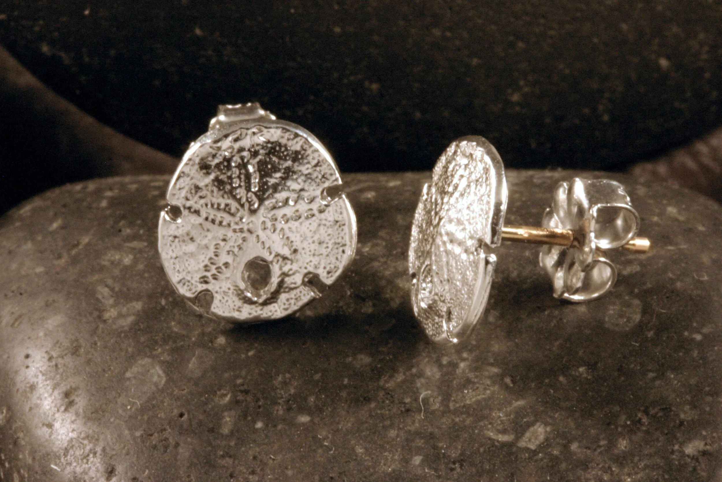 A side view of sterling silver mini sanddollar stud earrings with 14K gold posts.