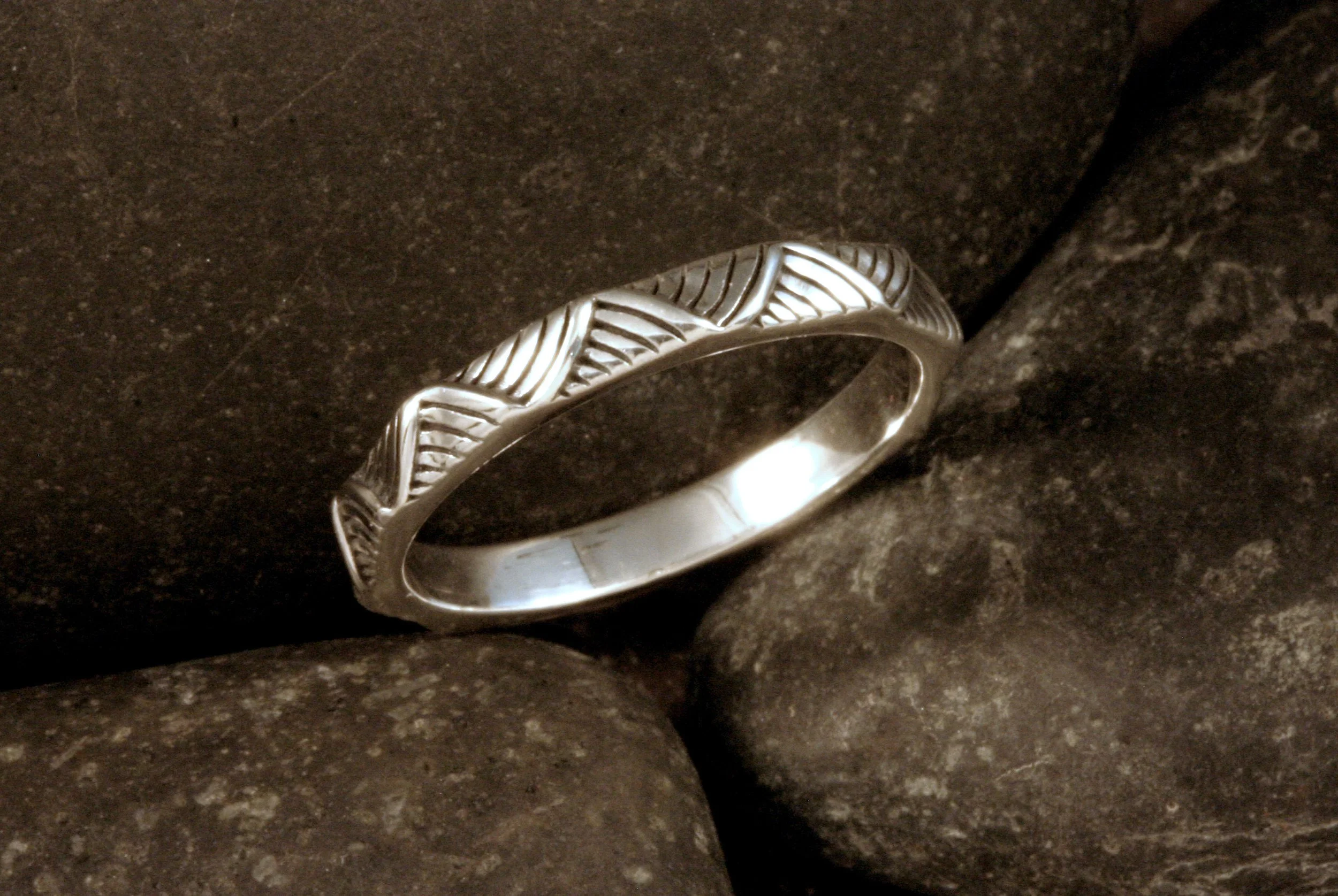 An oxidized sterling silver stackable band with a curved angled stripes pattern.