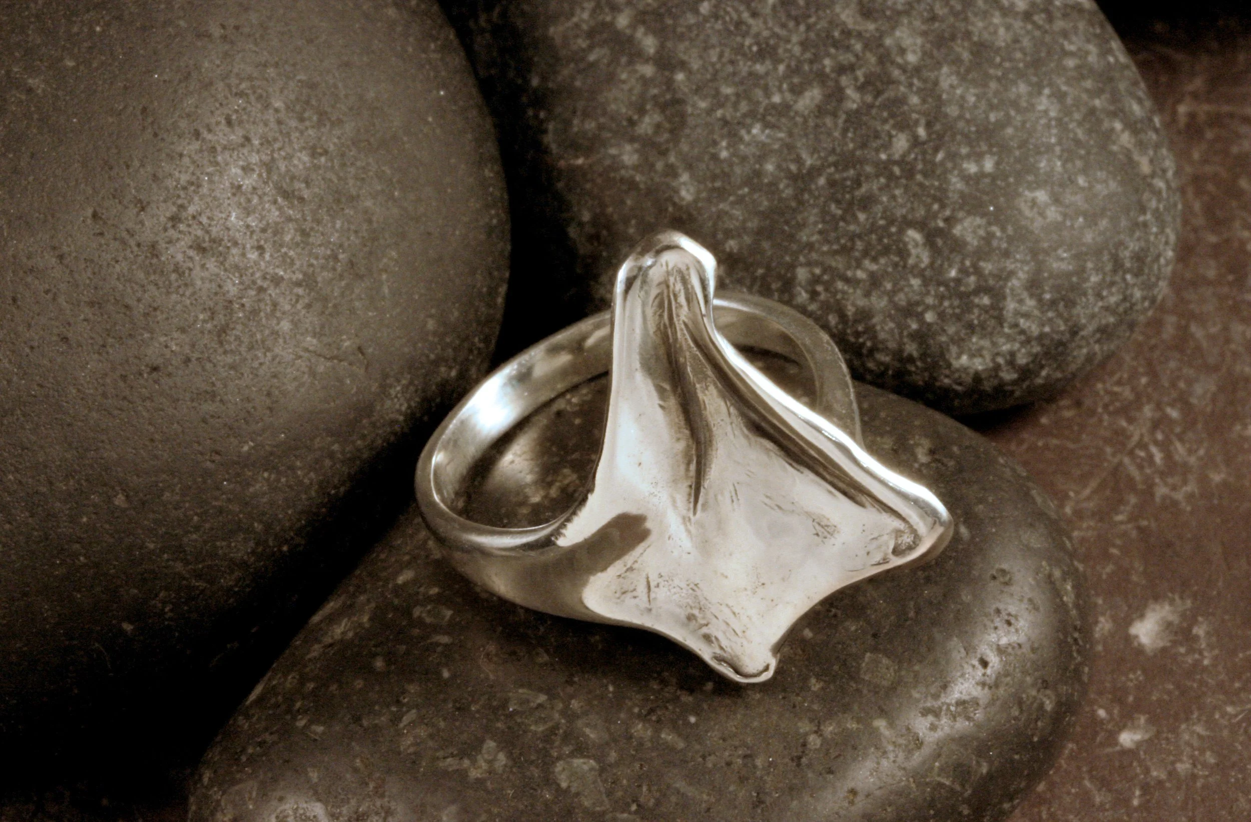 An oxidized sterling silver artsy kite triangle shaped ring sitting on its side atop a stone.