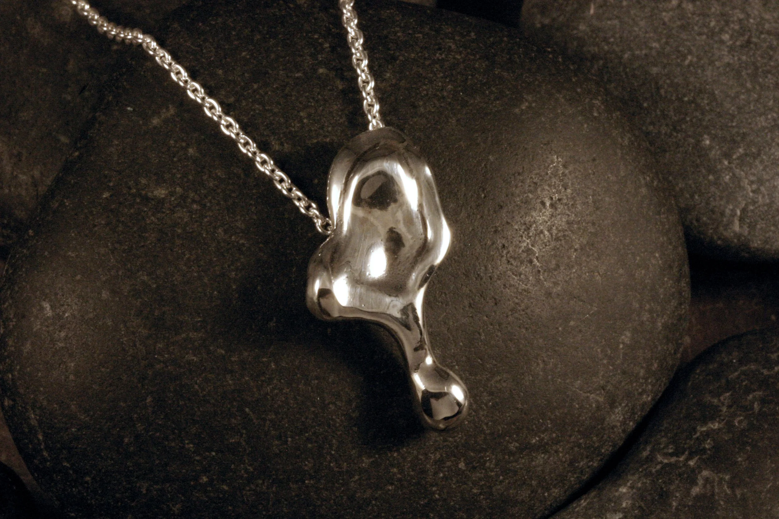 An oxidized sterling silver freeform petal drop pendant angled atop a stone.