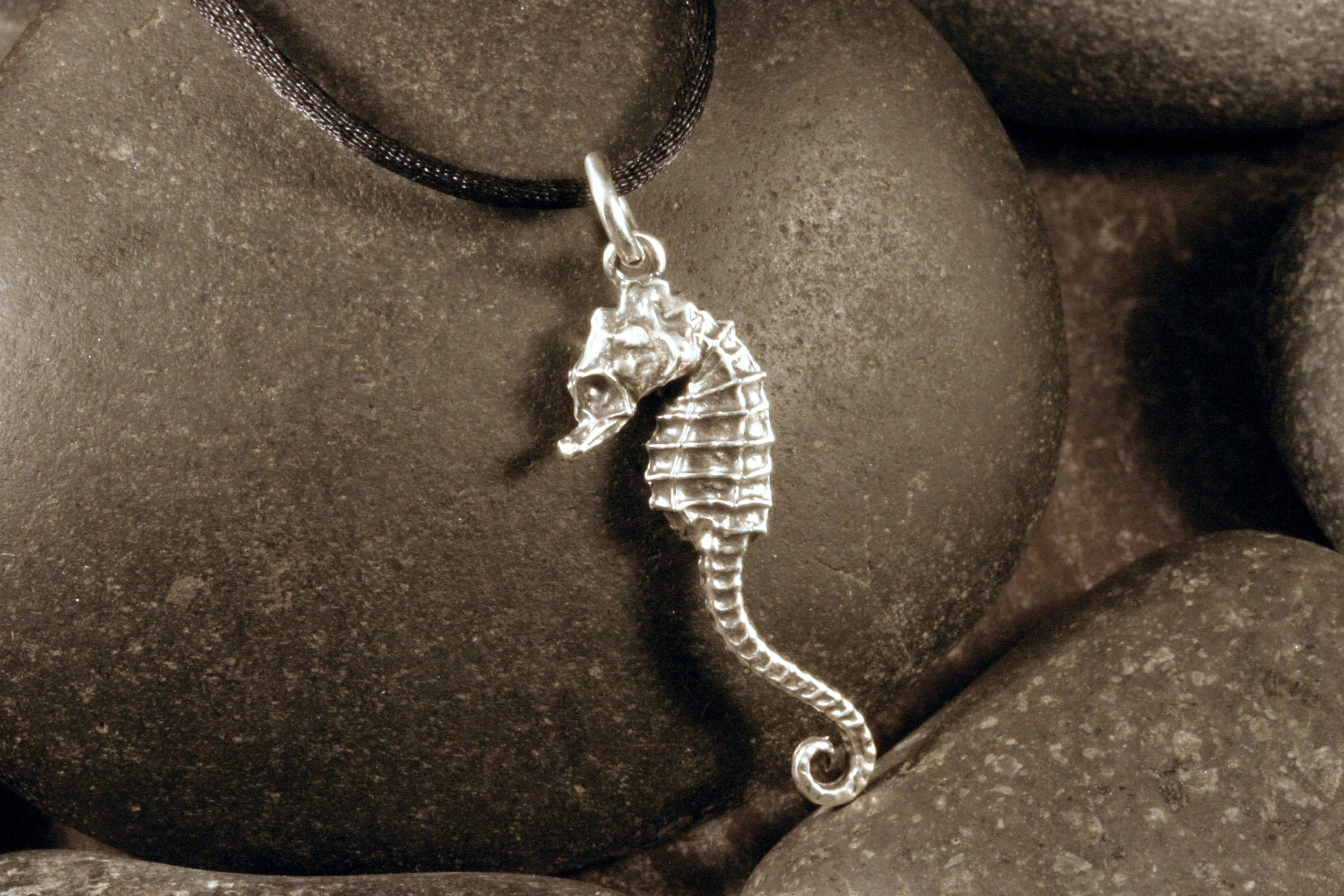 A side view of an oxidized sterling silver seahorse charm with a long tail.