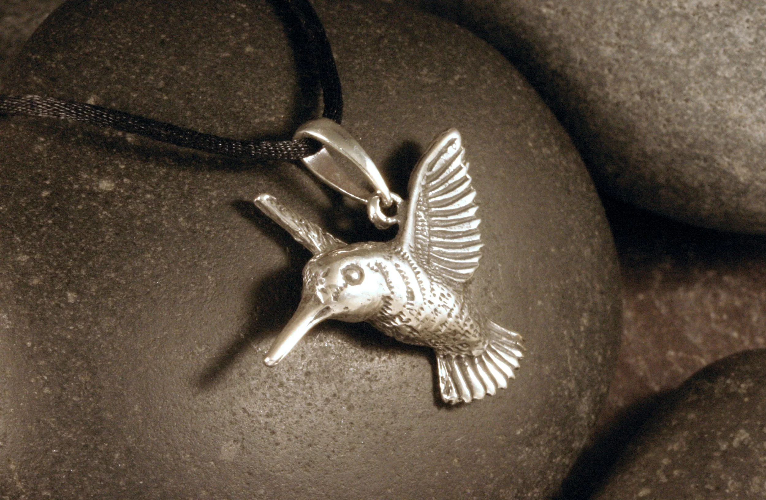 A side view of a large oxidized sterling silver hummingbird pendant.