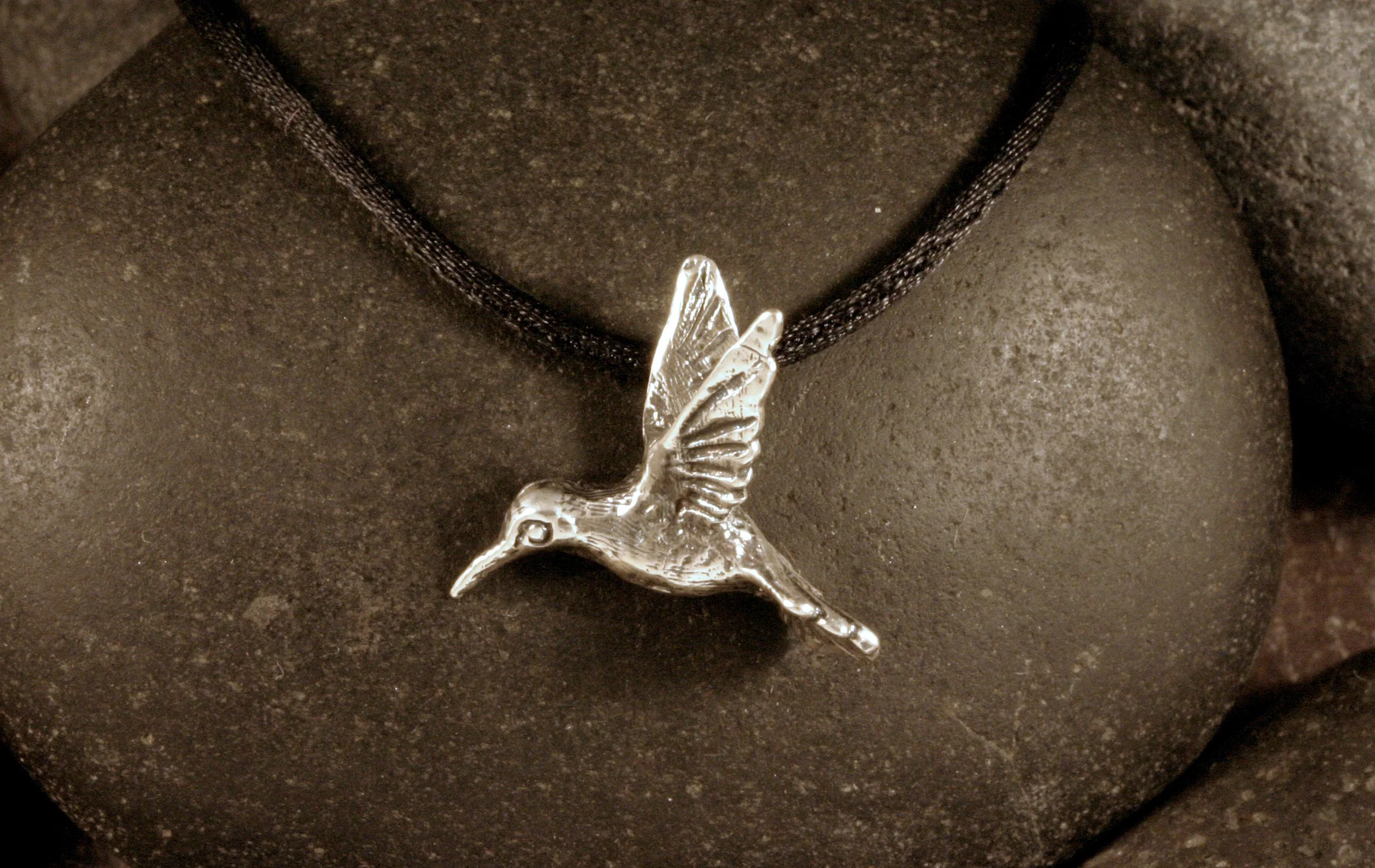 A front view of a small oxidized sterling silver 3-D hummingbird pendant.