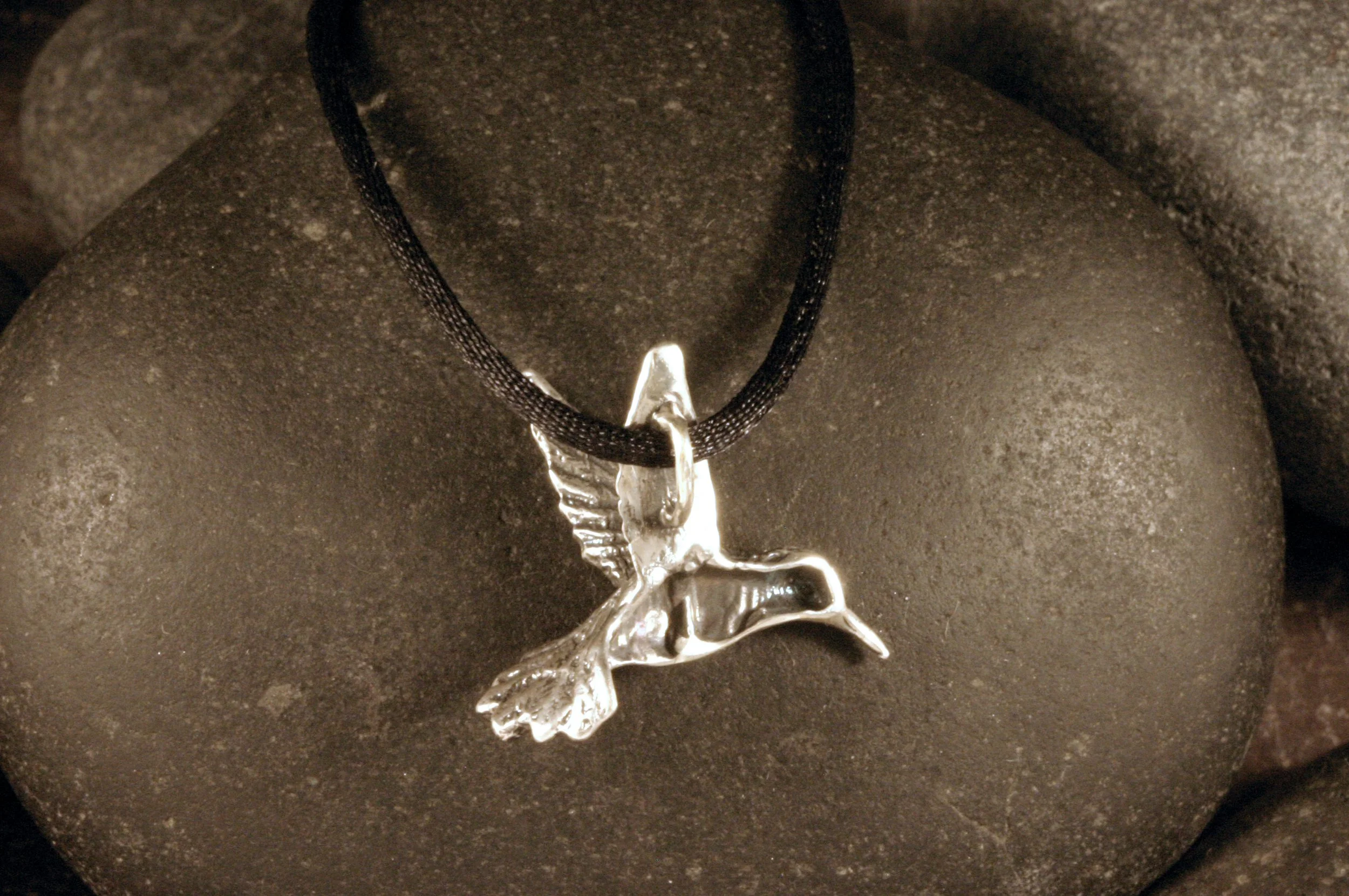 A back view of an oxidized sterling silver small hummingbird pendant.