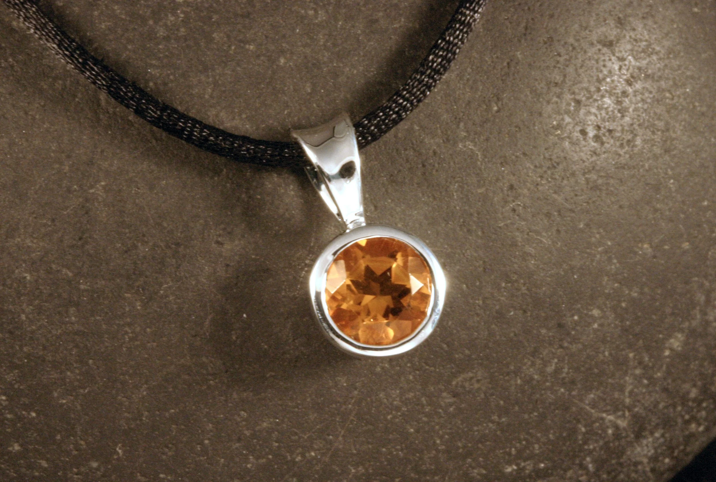 A sterling silver bezel set citrine pendant on a black cord.
