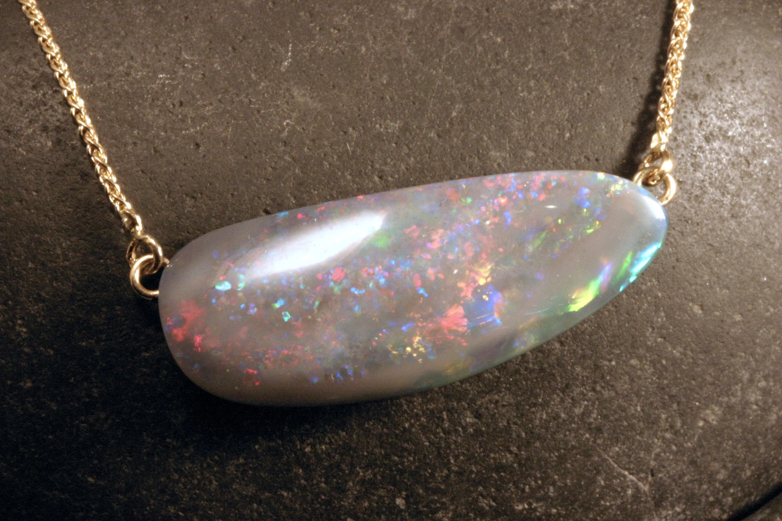 A close up of a 14K gold black Australian opal shell fossil necklace with a spiga chain.