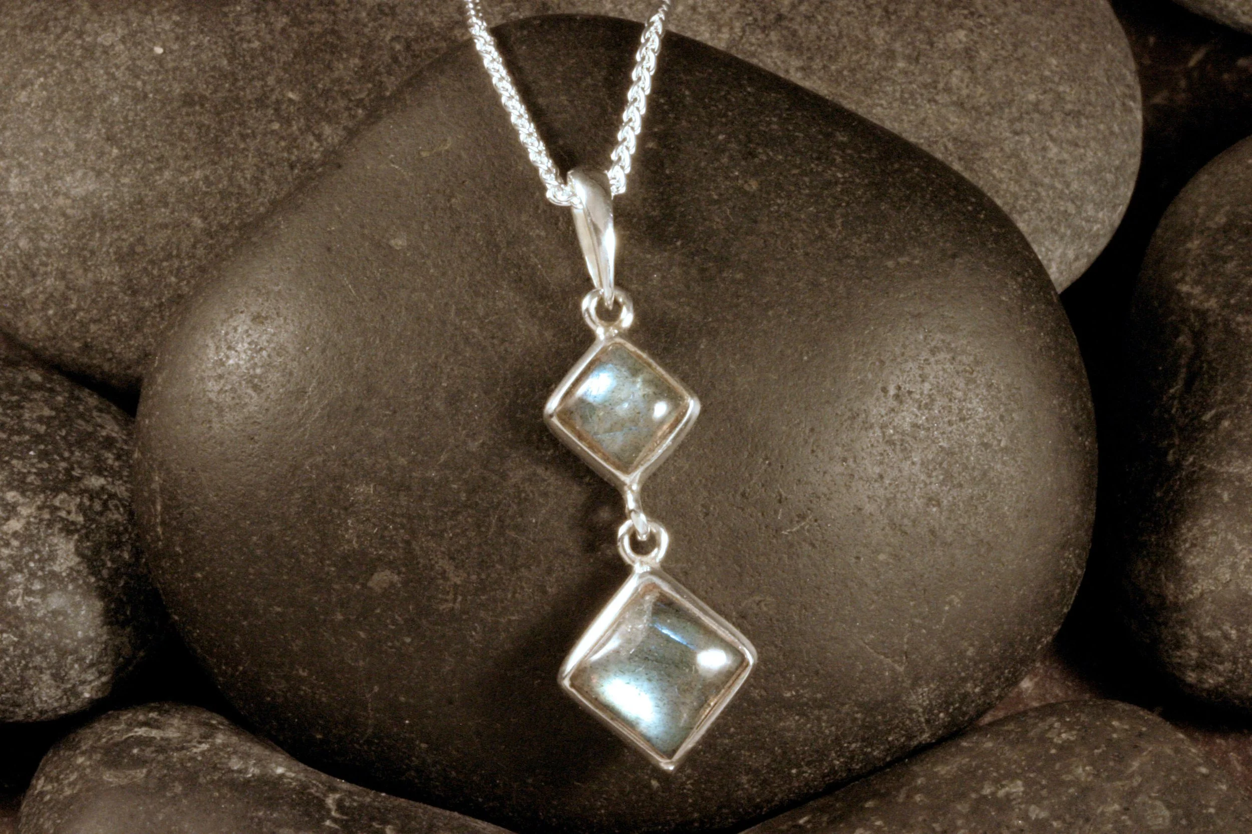 A front view of a sterling silver pendant with two bezel set labradorites in a square diamond cabochon cut.