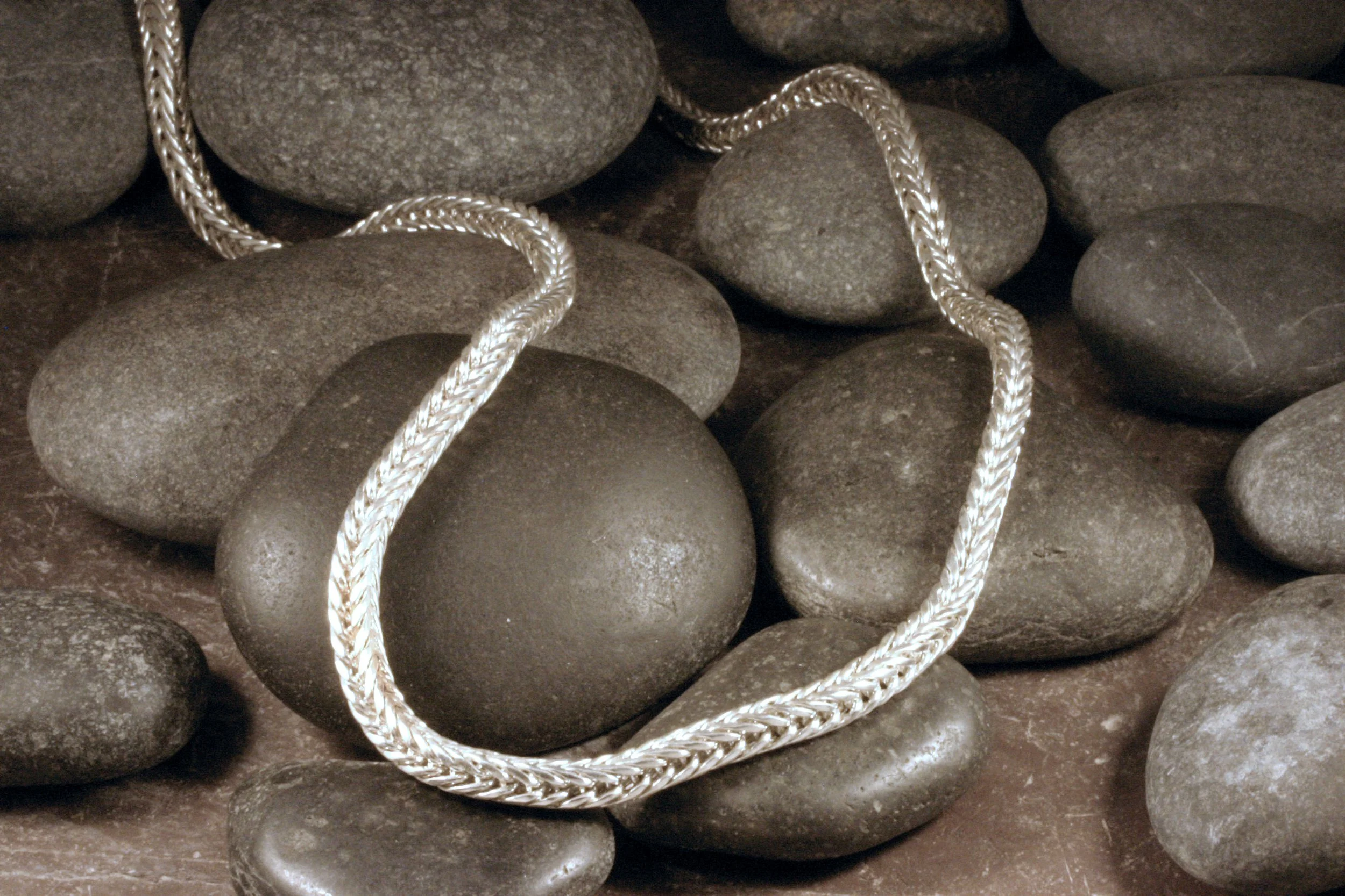 A sterling silver square double loop in loop chain necklace draped over a pile of rocks.