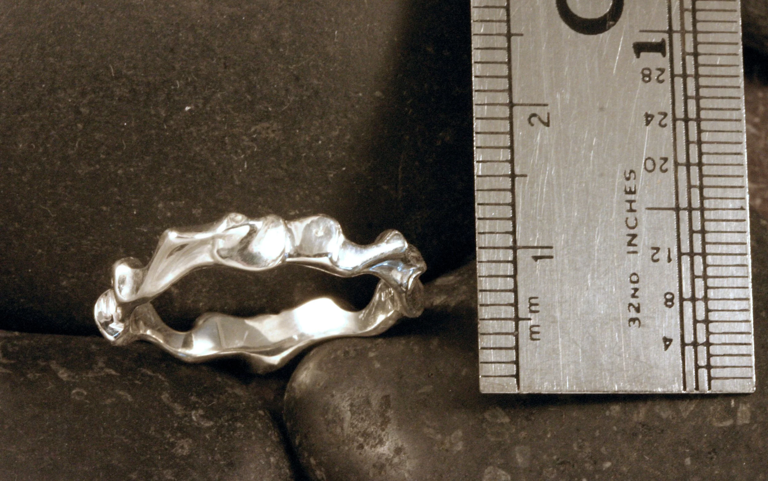 A funky freeformed patterned sterling silver ring next to a ruler.