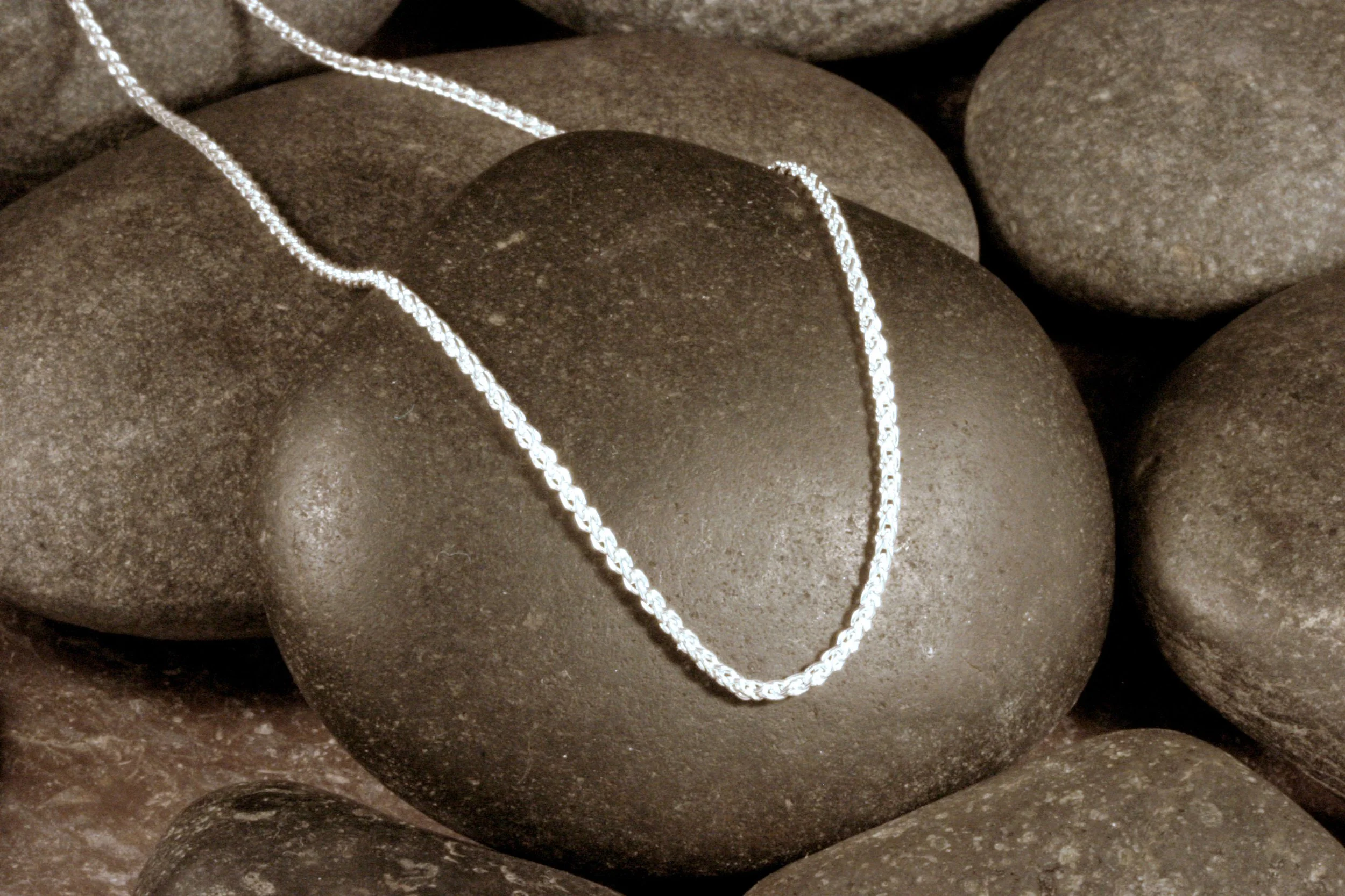 A sterling silver 1.5 mm spiga chain draped over a stone.