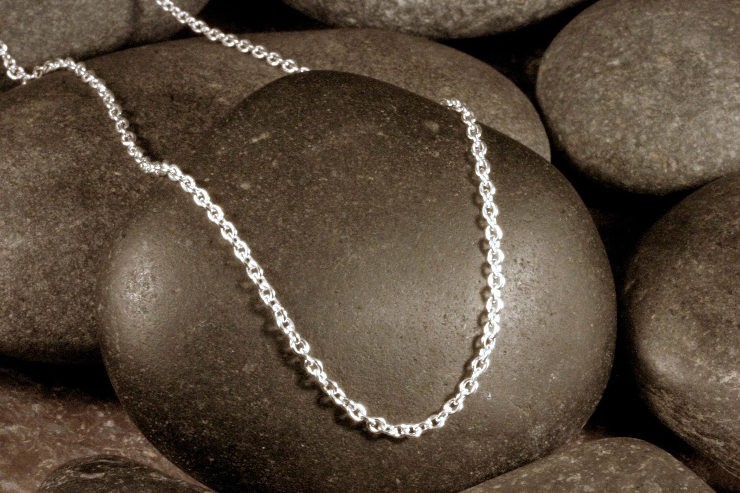 A sterling silver 1.95 mm cable chain draped on a stone.