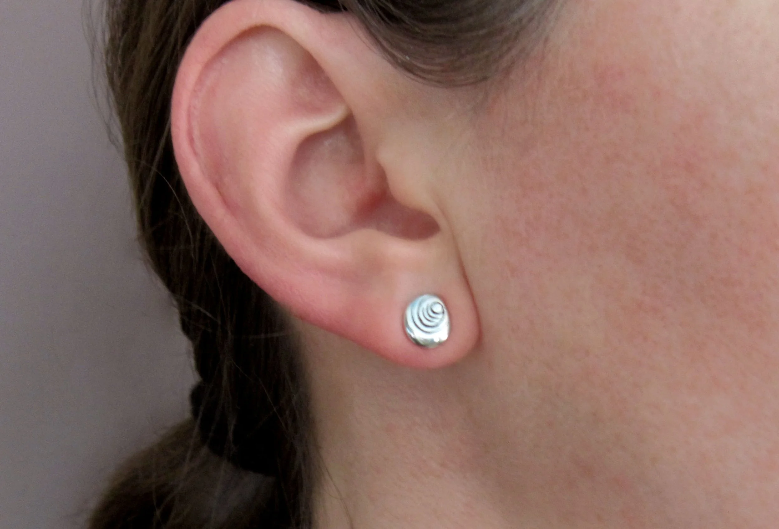 A model wearing sterling silver stud earrings with a dot ripple pattern.