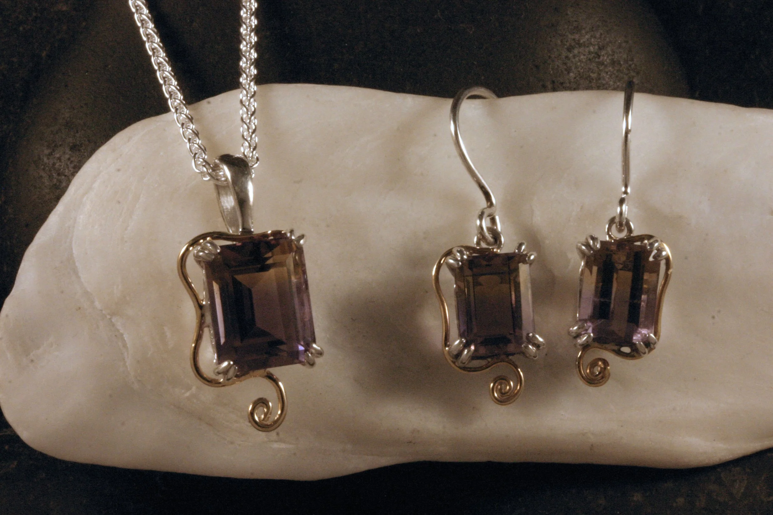 A matched jewelry set of a sterling silver & 14K gold ametrine pendant and earrings hanging on a shell stand.