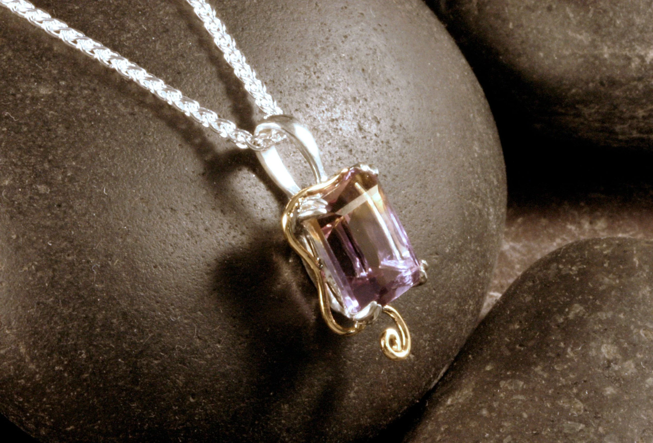 A side view of a sterling silver & 14K gold ametrine pendant with a double prong setting & a spiral design accent.