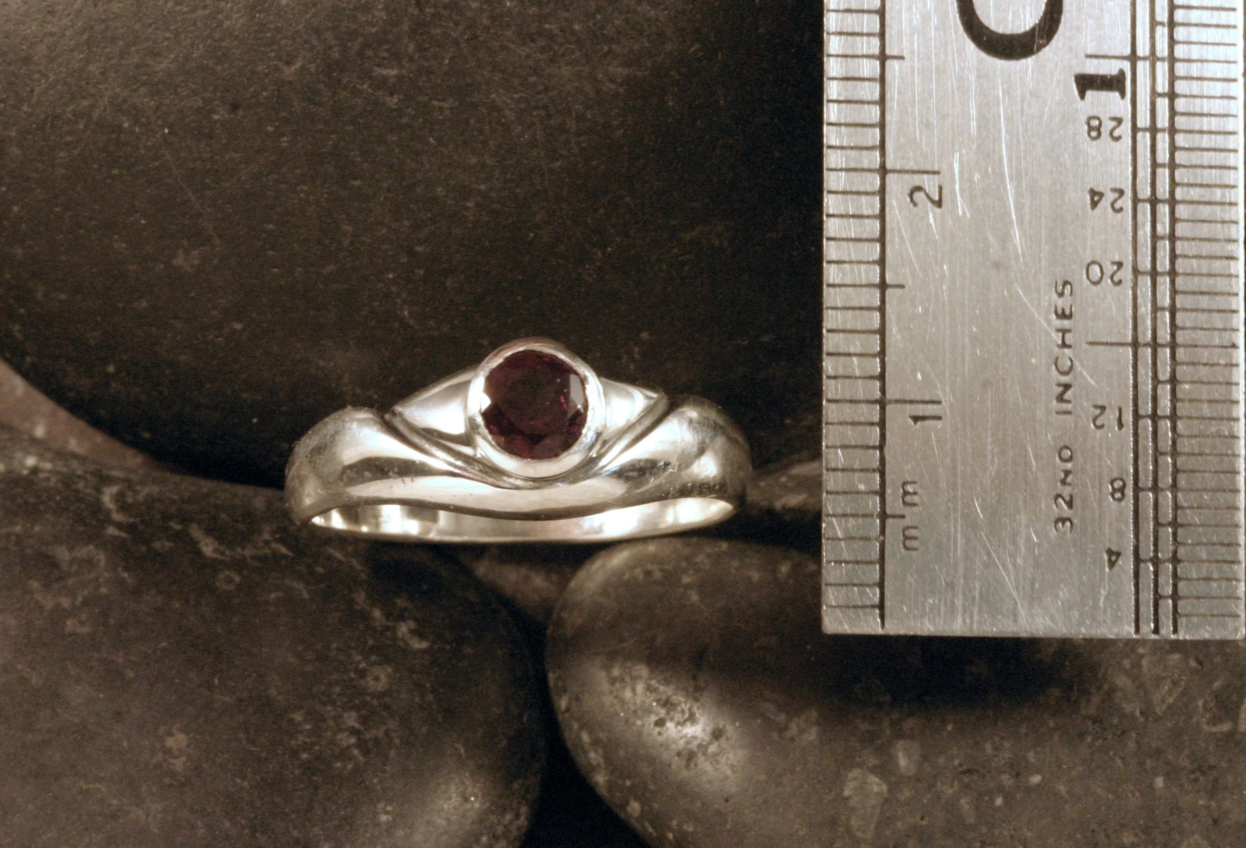 An oxidized sterling silver rhodolite garnet organic v ring next to a ruler.