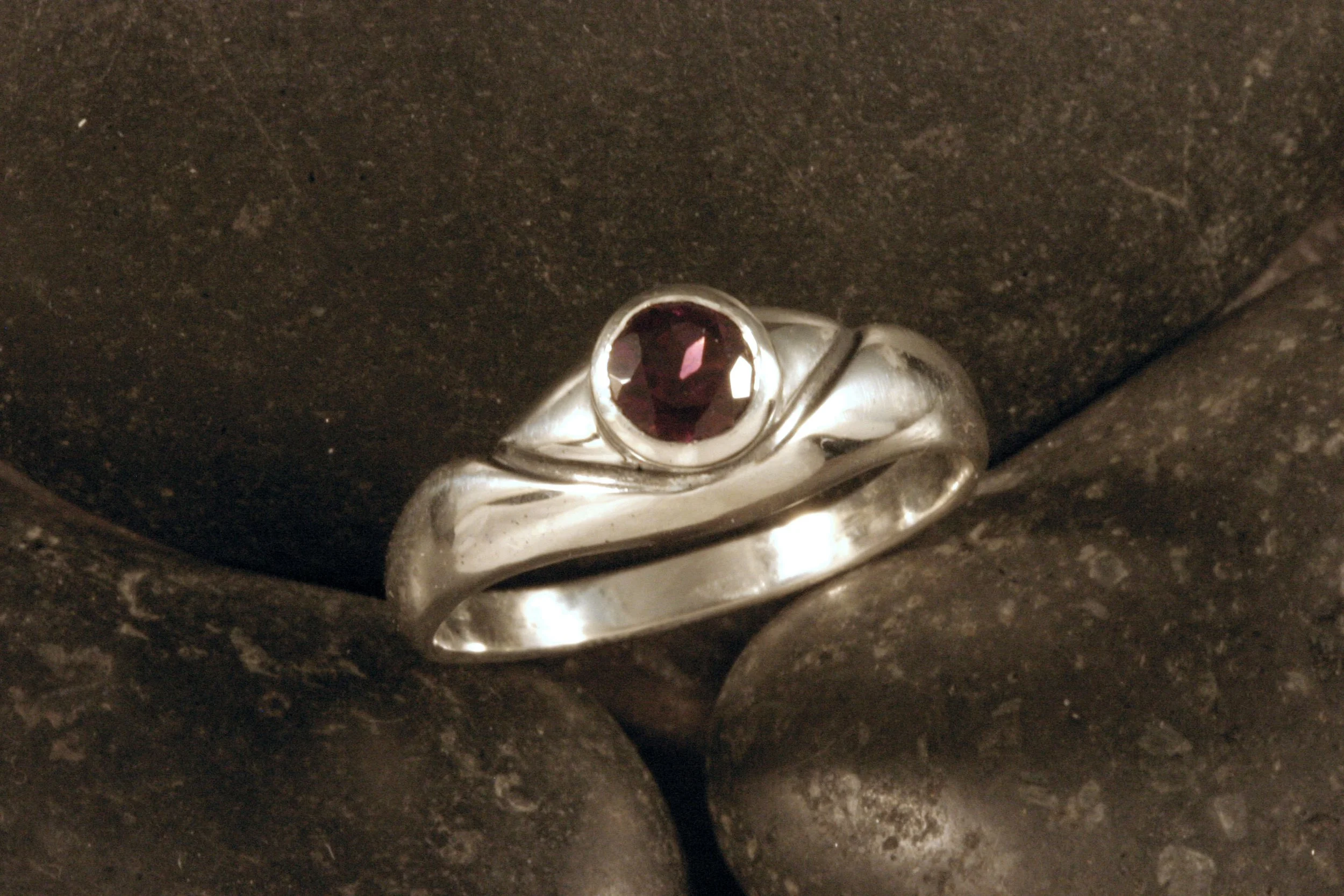 A three quarters view of an oxidized sterling silver organic v shaped ring with a bezel set rhodolite garnet.
