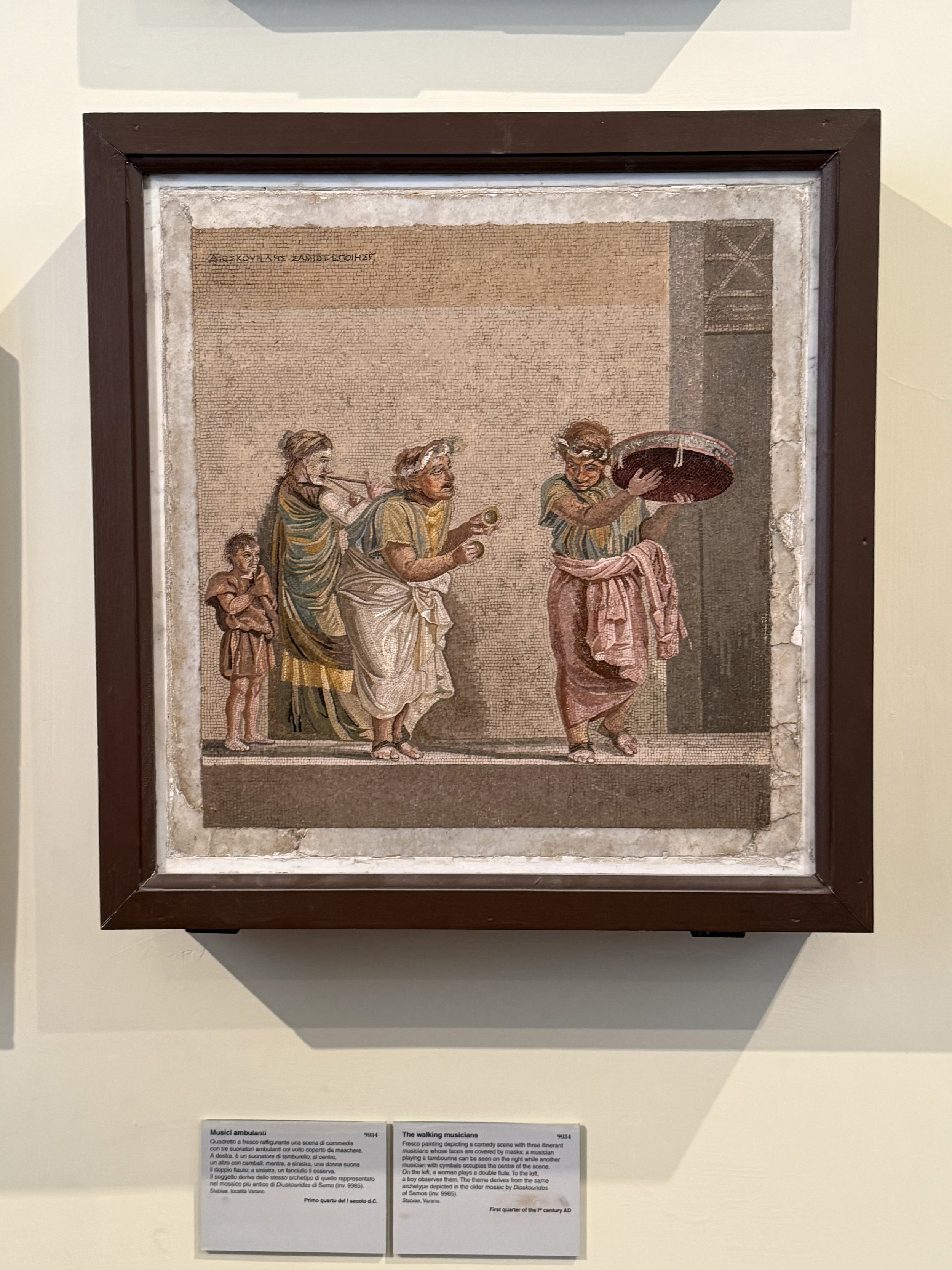 Ancient mosaic artwork depicting three young men possibly musicians or dancers, illustrated with detailed clothing and hairstyles, framing a scene of cultural or social significance.