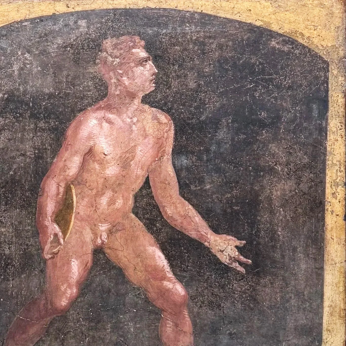 Ancient Roman fresco of a nude male figure walking left, with detailed muscular features, set against a dark background and framed with a gold border.