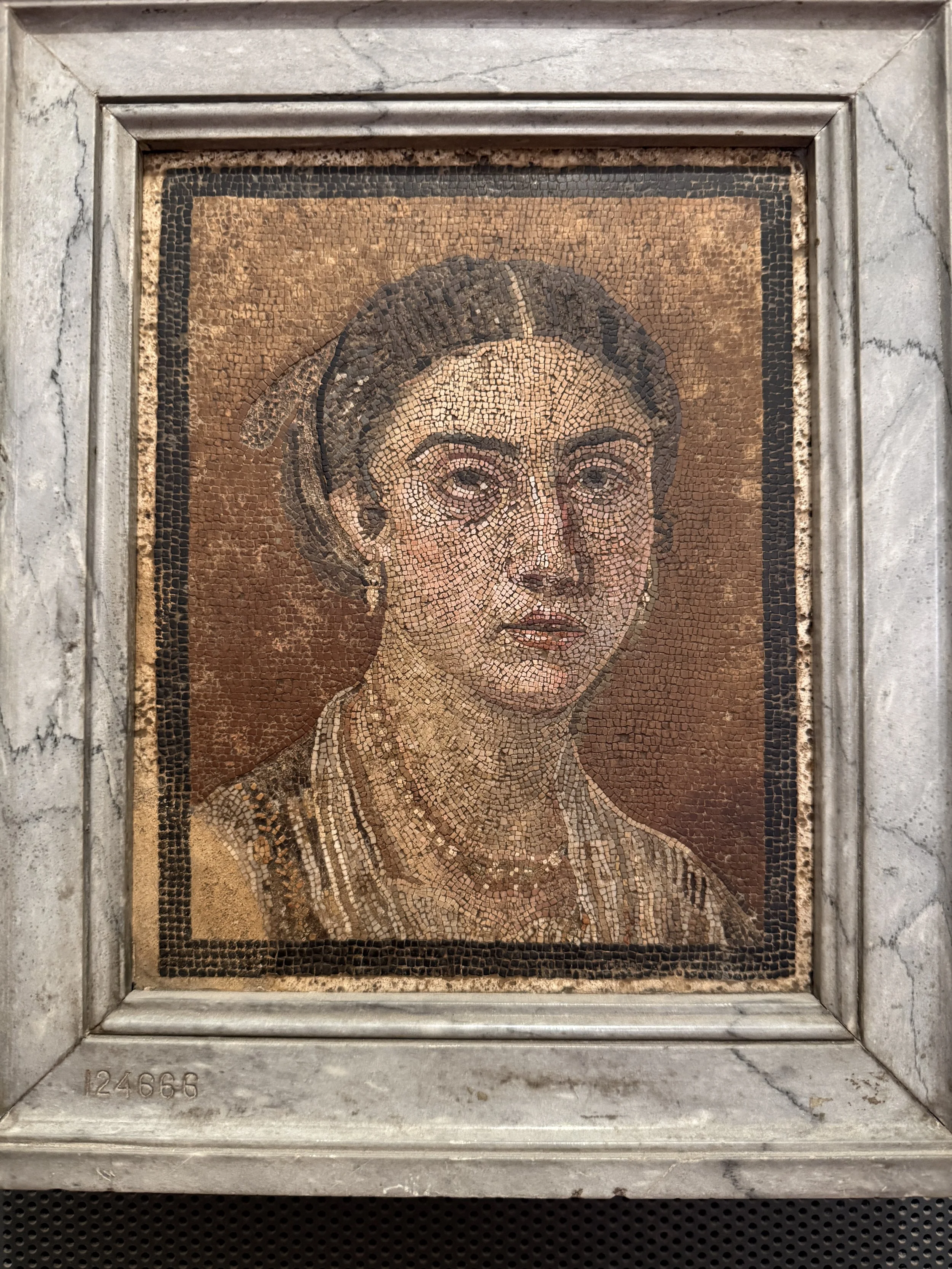 Ancient mosaic portrait of a woman with head covering, framed in stone.