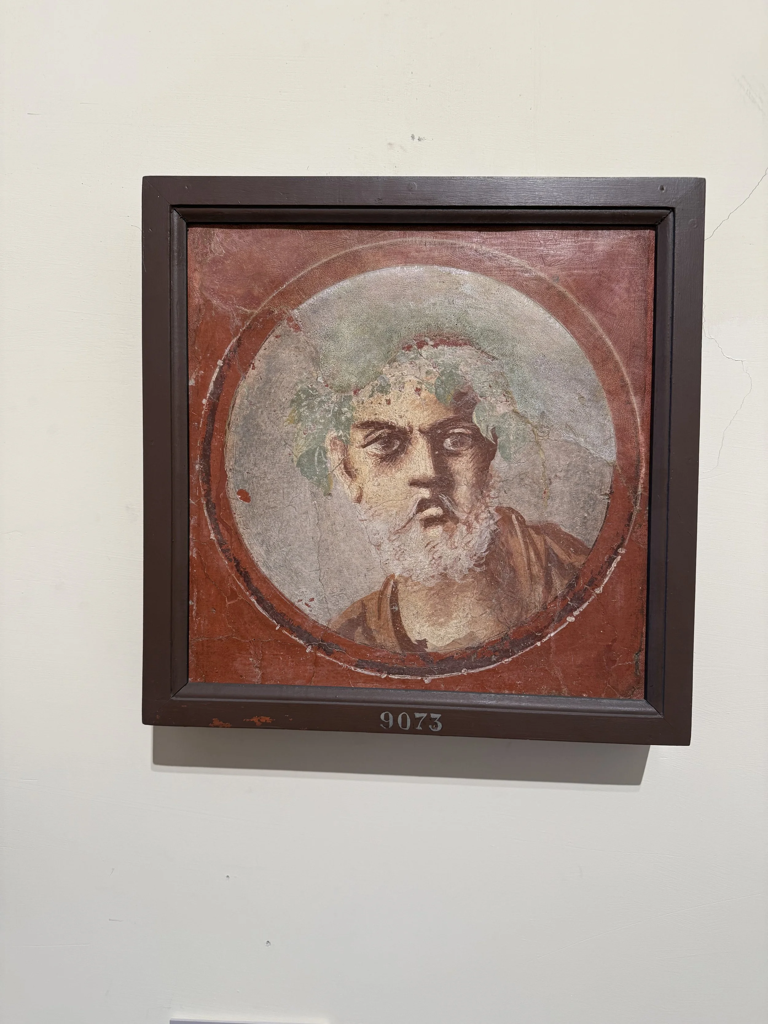 A framed, ancient religious icon painting depicting a bearded man with a halo, possibly Jesus Christ, on a red background with a cracked and aged surface, numbered 9073 at the bottom, hanging on a white wall.
