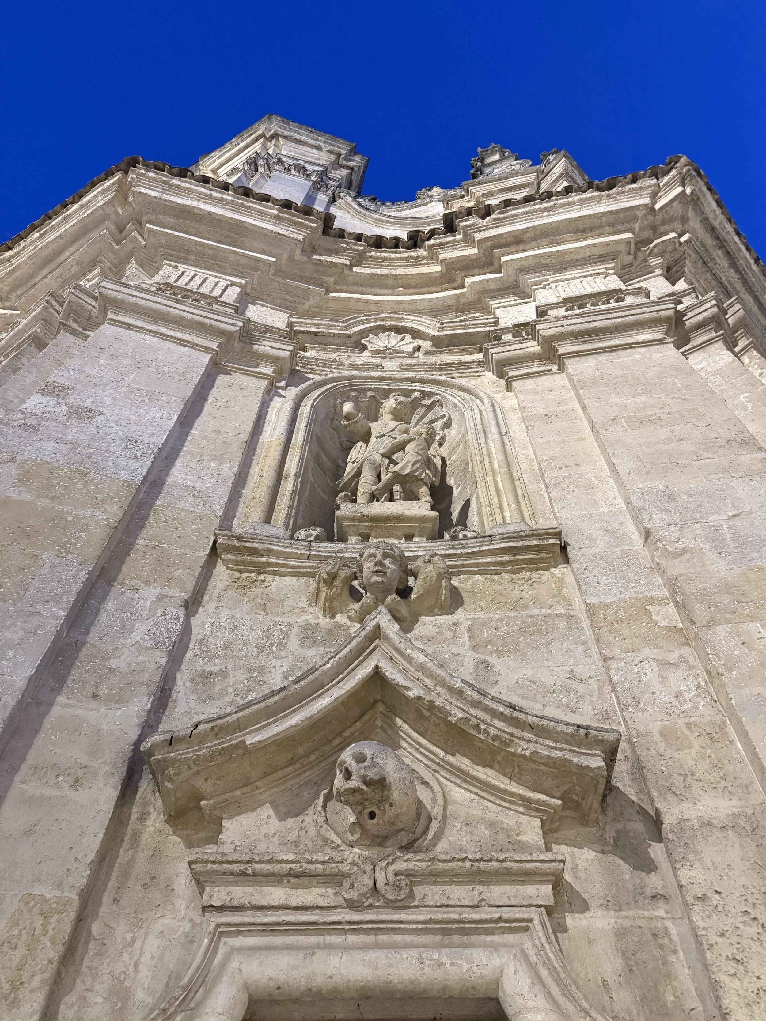 Low angle view of an ornate stone church or cathedral facade with sculptures and architectural details against a clear blue sky.