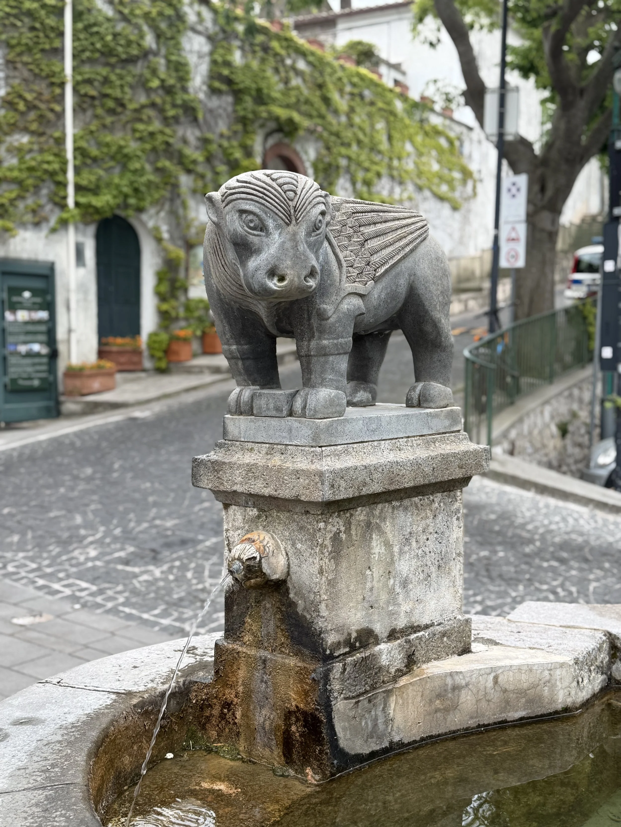 A stone fountain with a carved lion-headed spout, water flowing into a small basin.