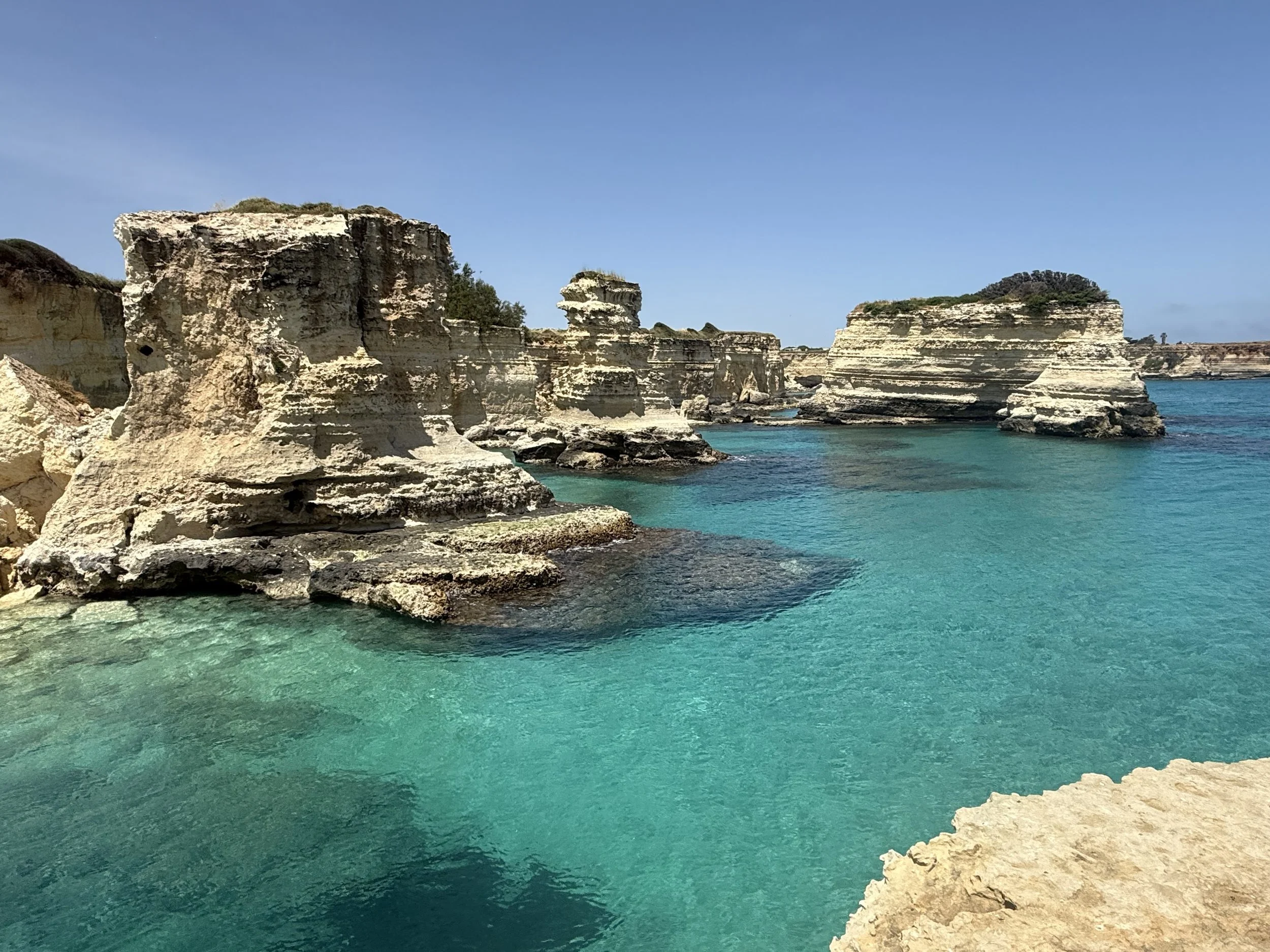 Cliffs and rock formations along a turquoise sea under a clear blue sky.