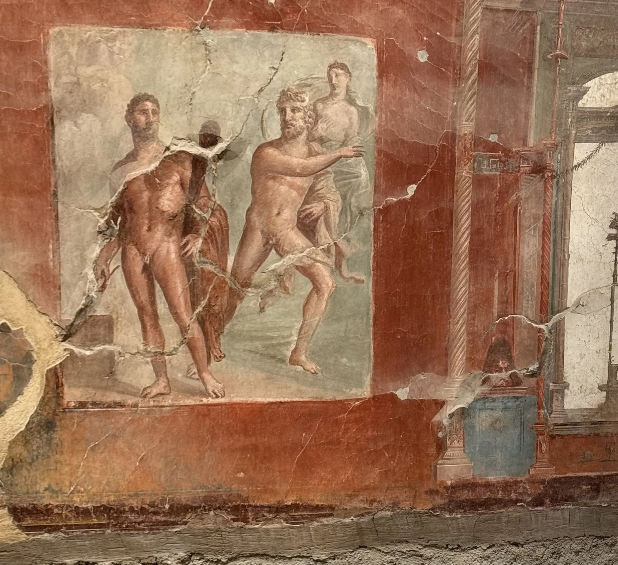 Ancient wall painting depicting human figures with a red background, some sections damaged or cracked.