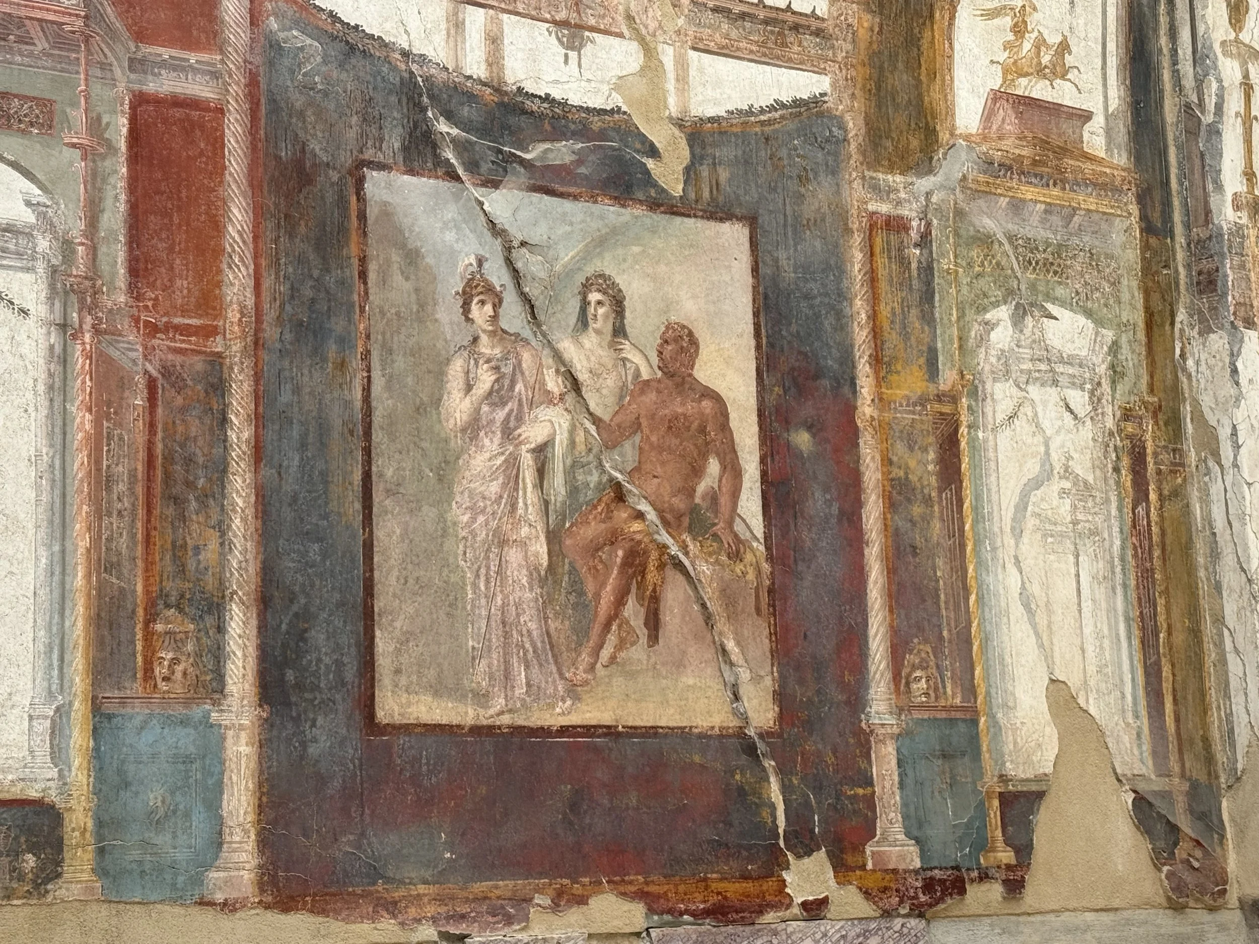 Ancient Roman fresco painting depicting two women in classical attire and a male figure, set within an ornate architectural interior.