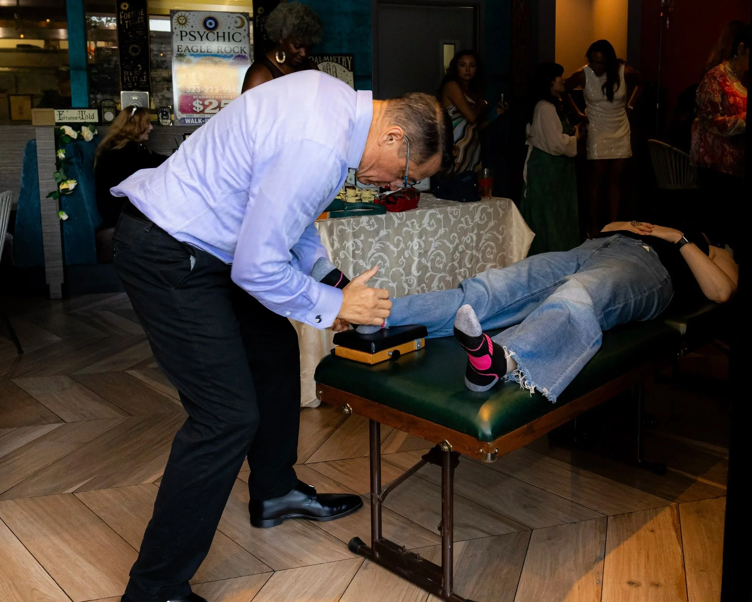 Man performing a stage magic trick with a woman lying on a table at a psychic-themed event