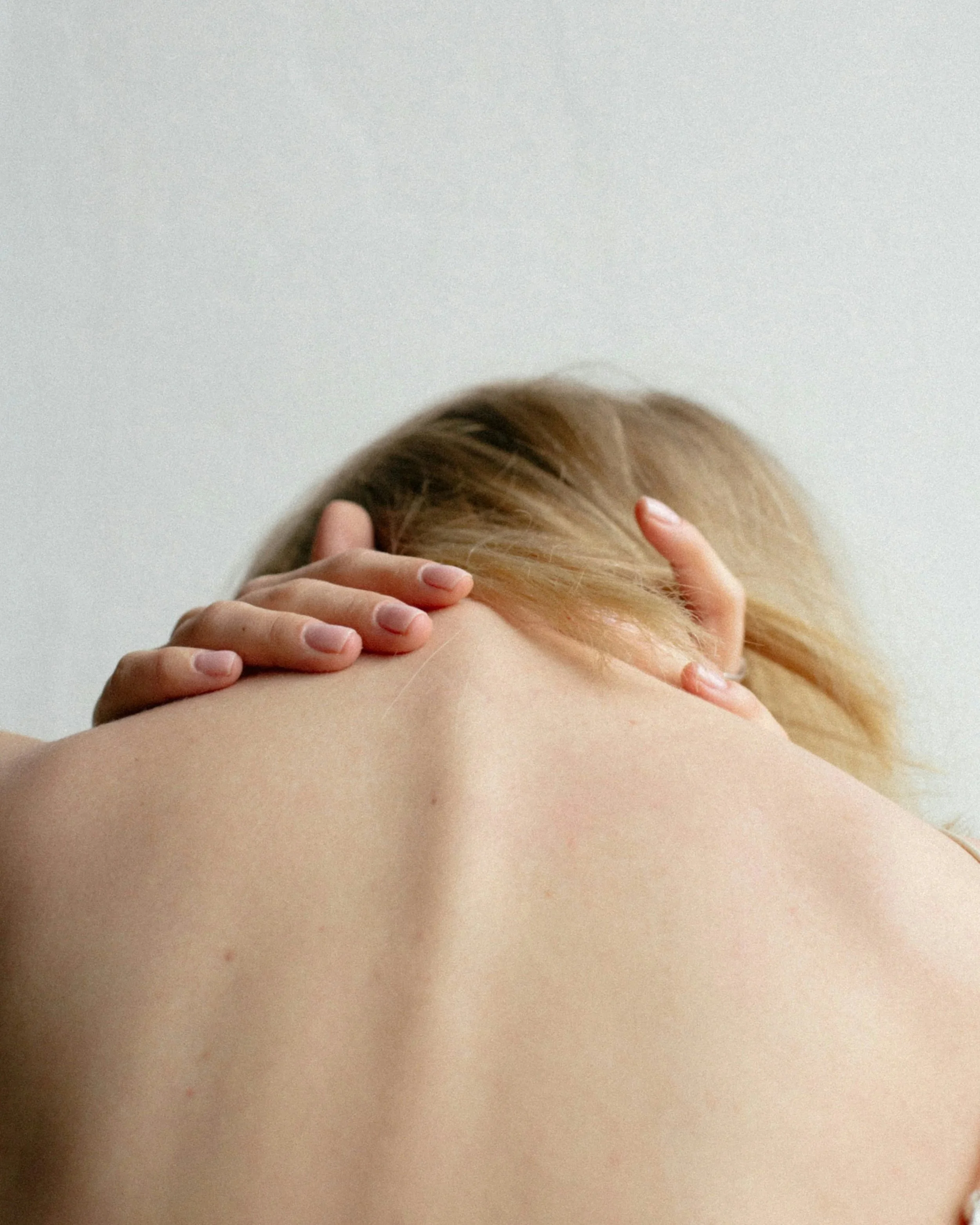 Close-up of a person with long blonde hair lying face down while another person gently parts their hair with manicured hands.