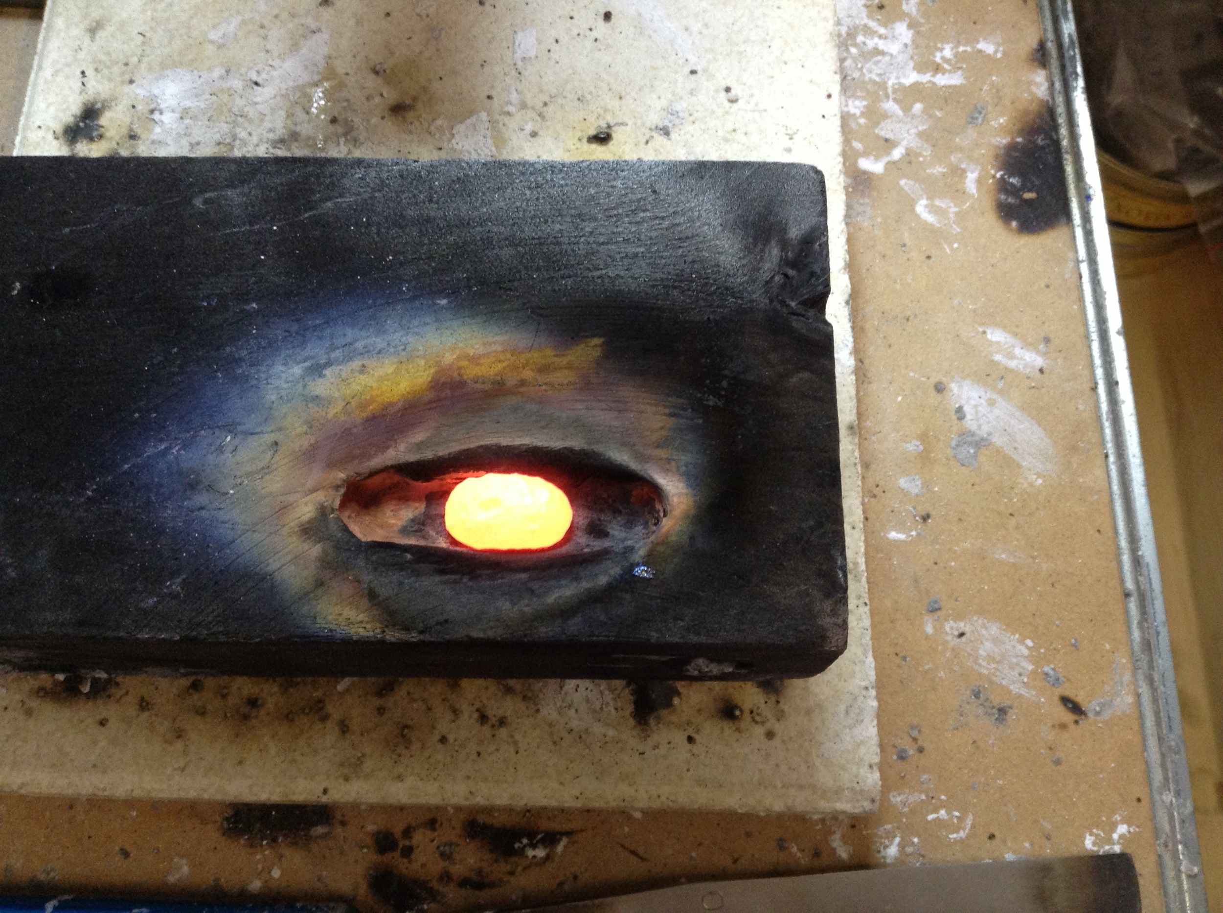 Glowing hot ingot, fresh metal to use made from scrap and offcuts. Melted into a charcoal block.