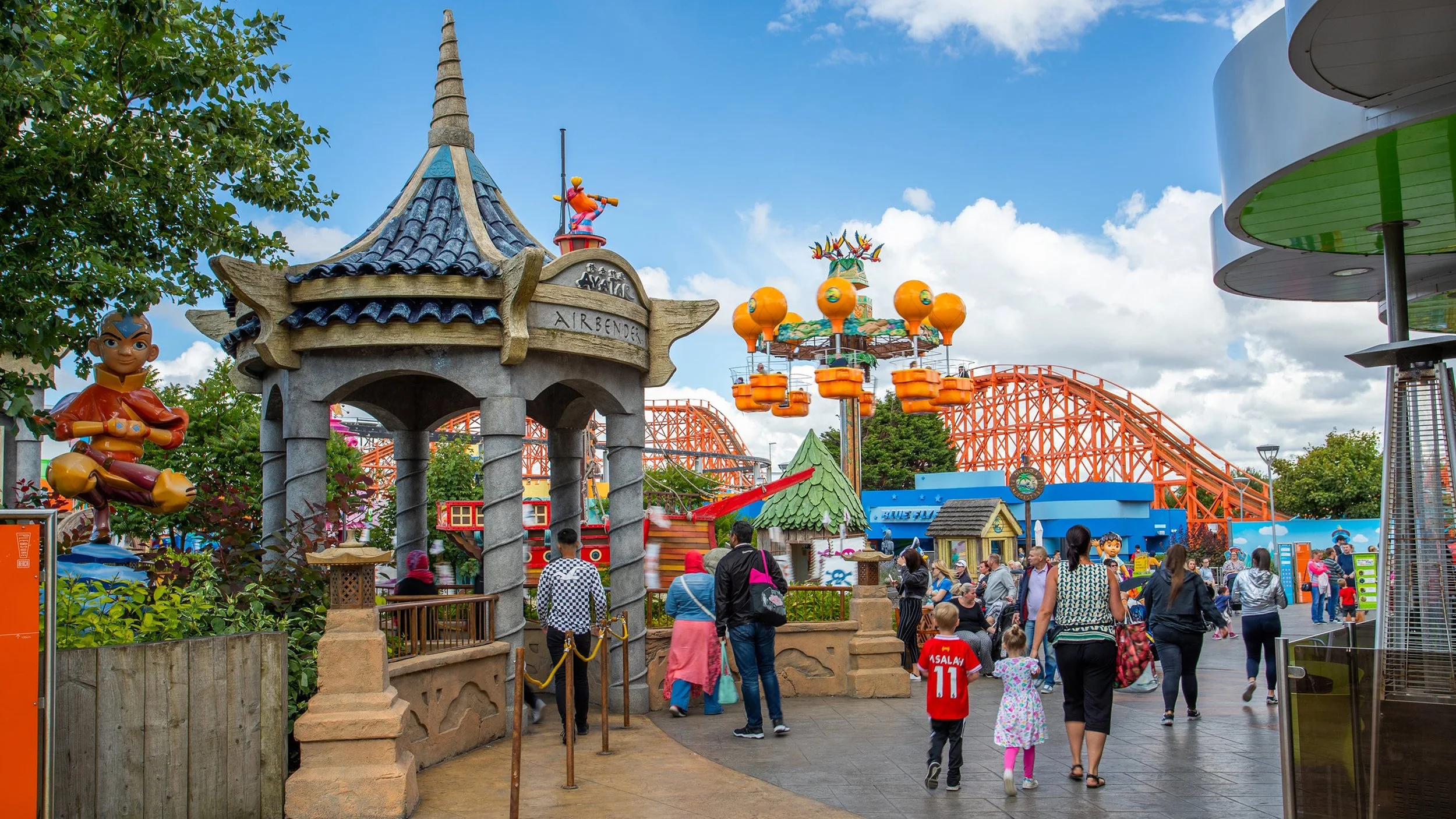 pic showing Nickleodeon Land in Blackpool Pleasure Beach theme park - shows Avatar: The Last Airbender ride alongside parts of Dora the Explorer and other cartoon rollercoaster rides. It is a vibrant and busy space, full of people.