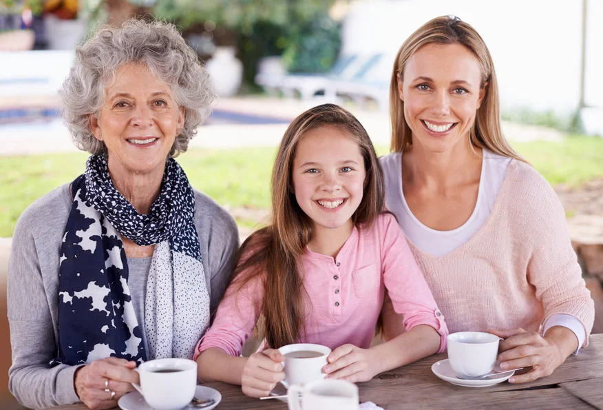 Three generations of females drinking tea outdoors and smiling at the camera