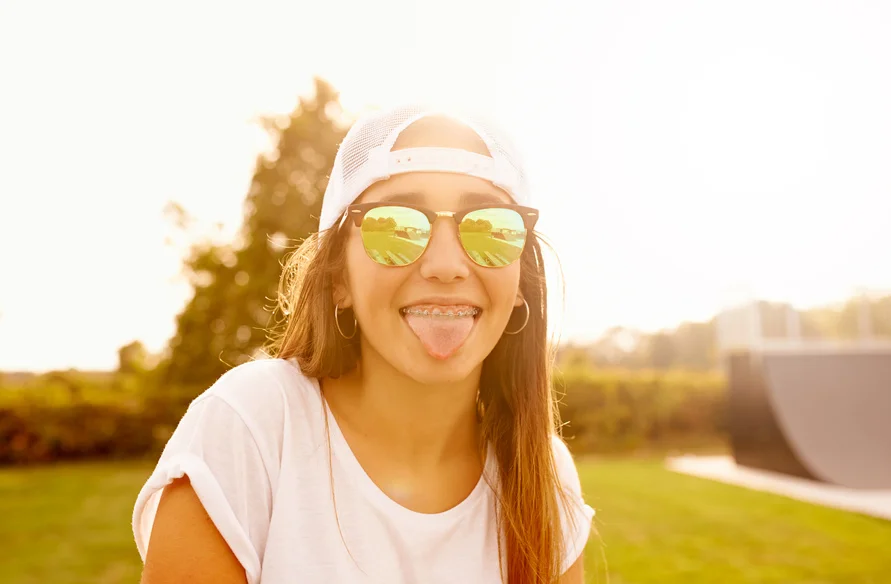 Girl with sunglasses, tongue sticking out and braces on teeth