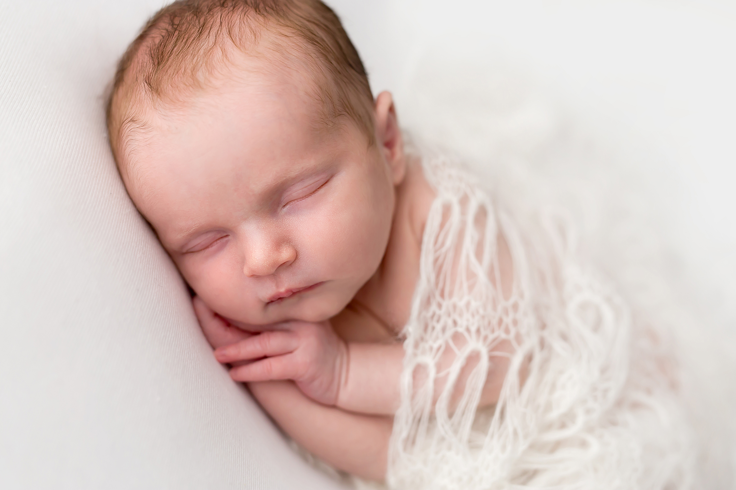 Melbourne newborn photographer has taken a photo of a baby girl sleeping on her side and covered in a knitted blanket.