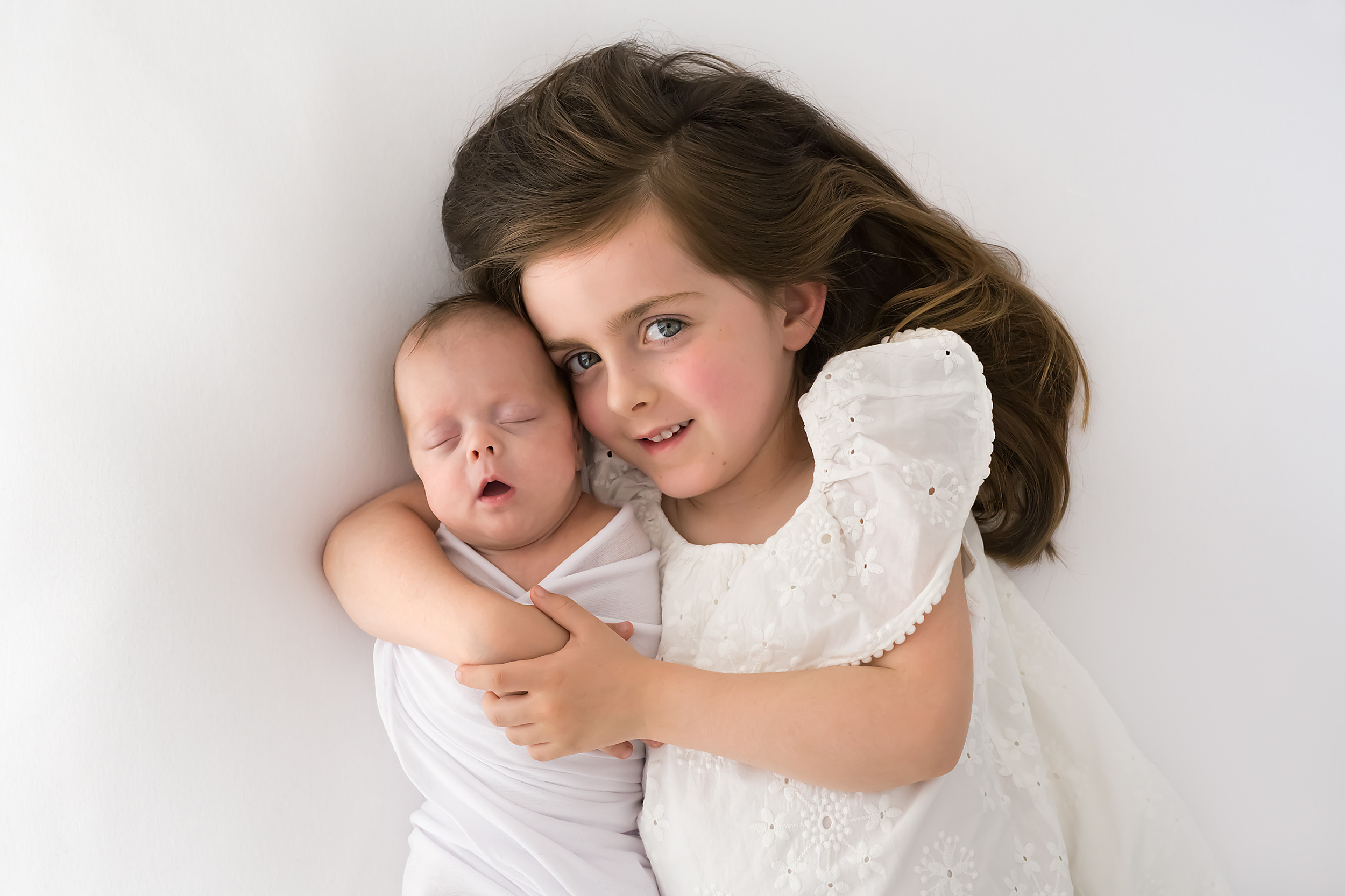 A professional photo of a girl cuddling her newborn baby sister during a photography session in Melbourne