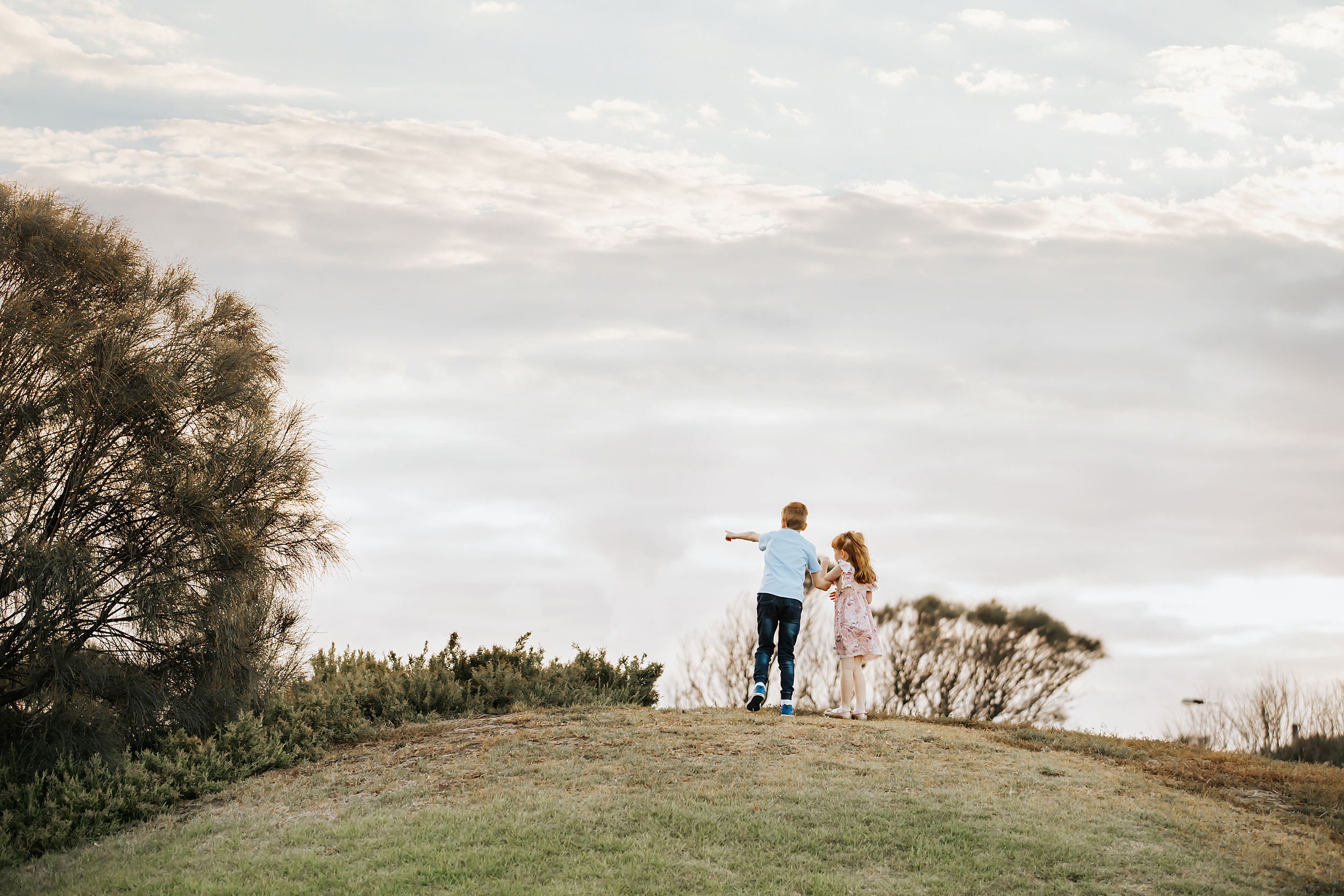 A candid photograph of two children standing at the top of a hill in Melbourne.  Taken by a professional photographer.