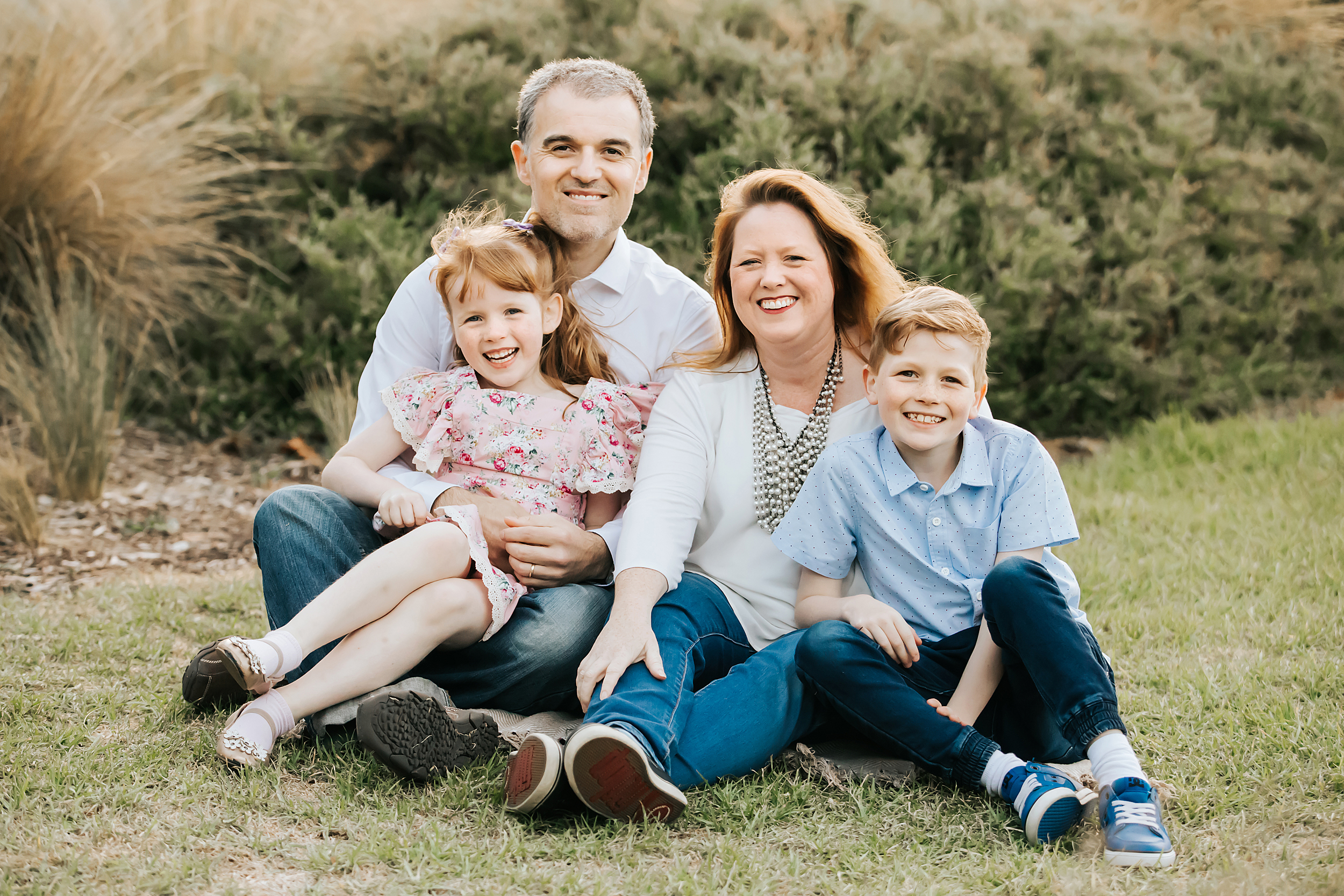 A natural family portrait of a family of four sitting on the grass during golden hour.  Taken by a Melbourne Family Photographer.