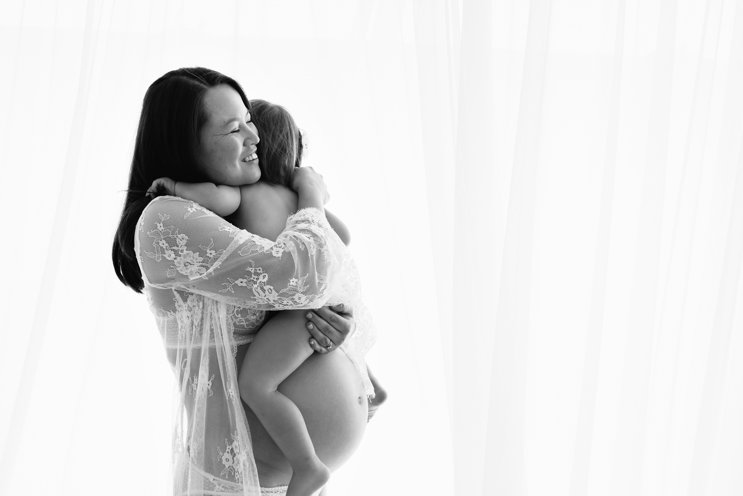 Black and white photo of pregnant mum cuddling her older daughter taken by professional photographer in Melbourne