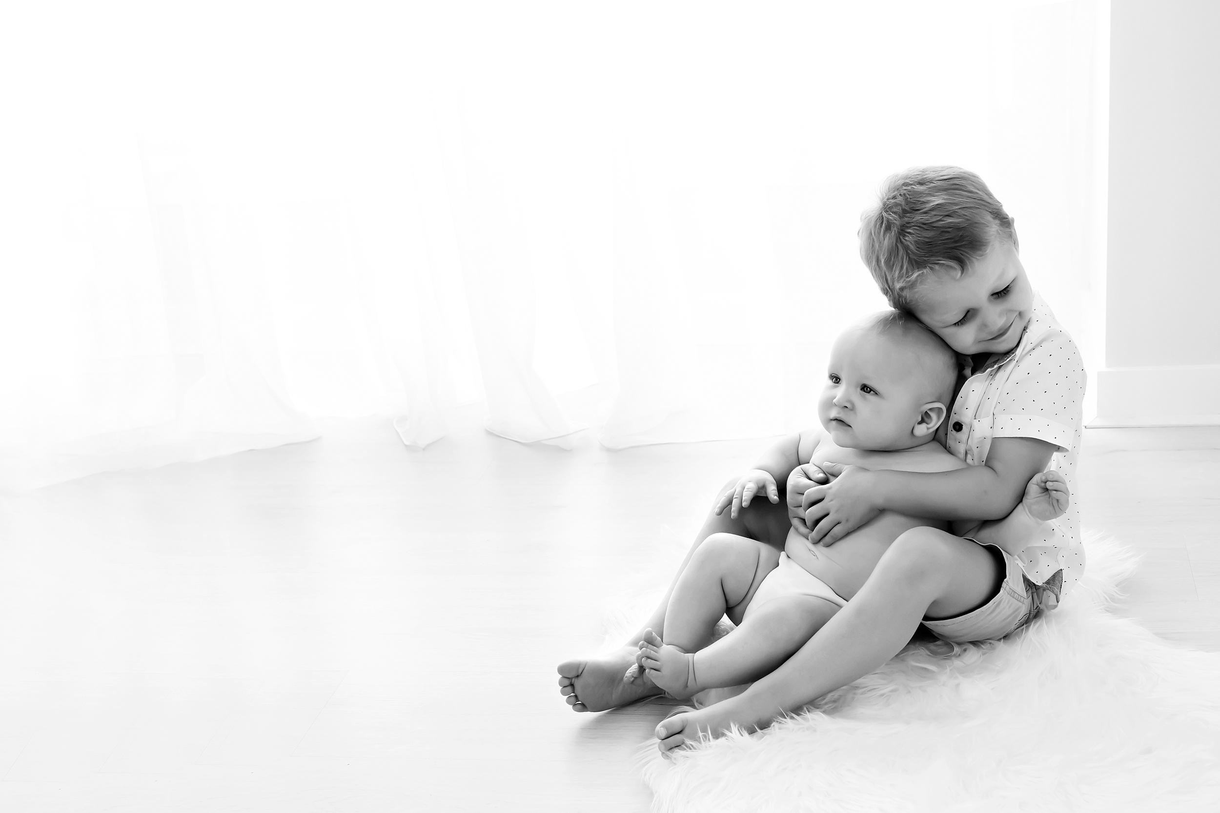 Black and white photo of older brother cuddling younger brother taken during baby photo session in Melbourne