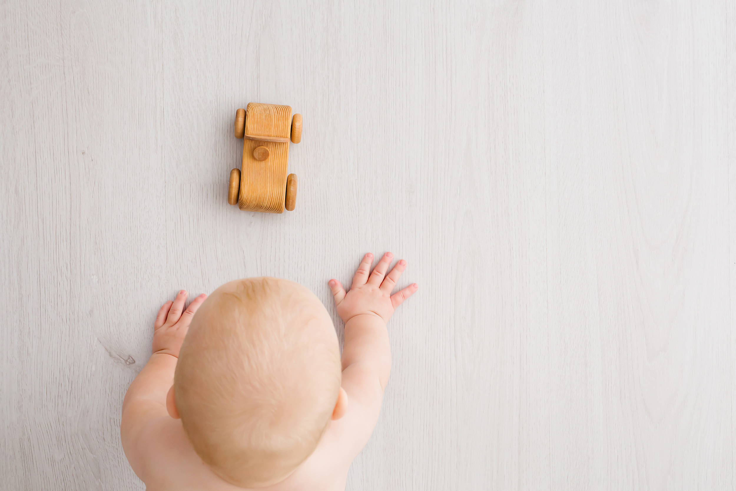 Image from above of baby crawling towards wooden car during baby milestone photography session in Melbourne