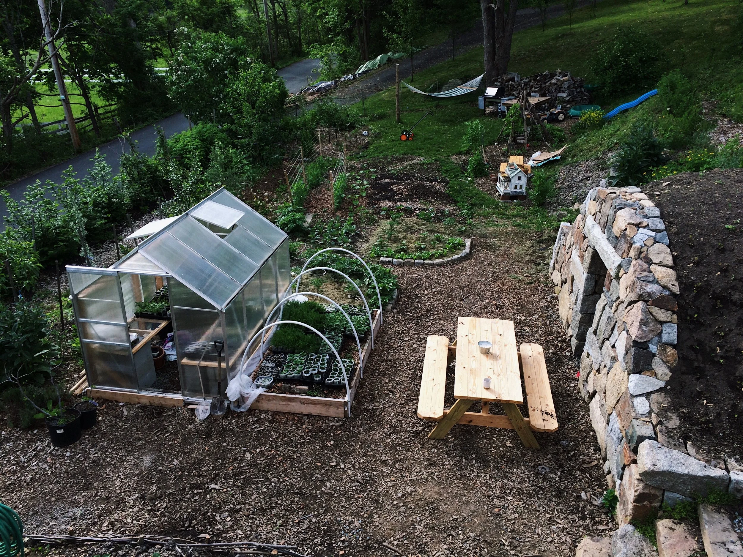 from the roof of the dinning room, a view of our little garden space out back. Greenhouse, raised bed / low tunnel. root cellar and stone stairs. To the left of the green house are the two orchard rows with hazelnuts, blackberries, raspberries, peaches, a dwarf cherry, grapes, goumi, seaberries and various other perennials including some strawberries. In the middle behind the greenhouse and extending back it the annual garden. Where the doll house, teepee and slide down the slope are all part of the children's garden. In the very back is a little lawn with our wood pile, the hammock and another fruit tree nursery bed for some of my grafted apples, a few cherries and some young american persimmons.Where the picnic table is is our gathering area...next year it will be grass / clover. Hoping to add a few more chairs and possible some string lights to cozy it up :)