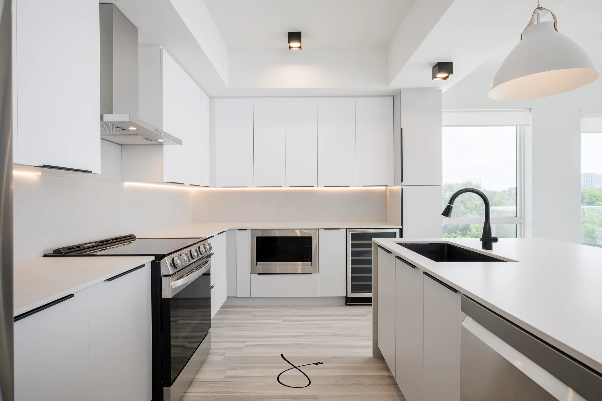 Modern white kitchen with black and stainless steel appliances, black faucet, large windows, and sleek minimalist design.